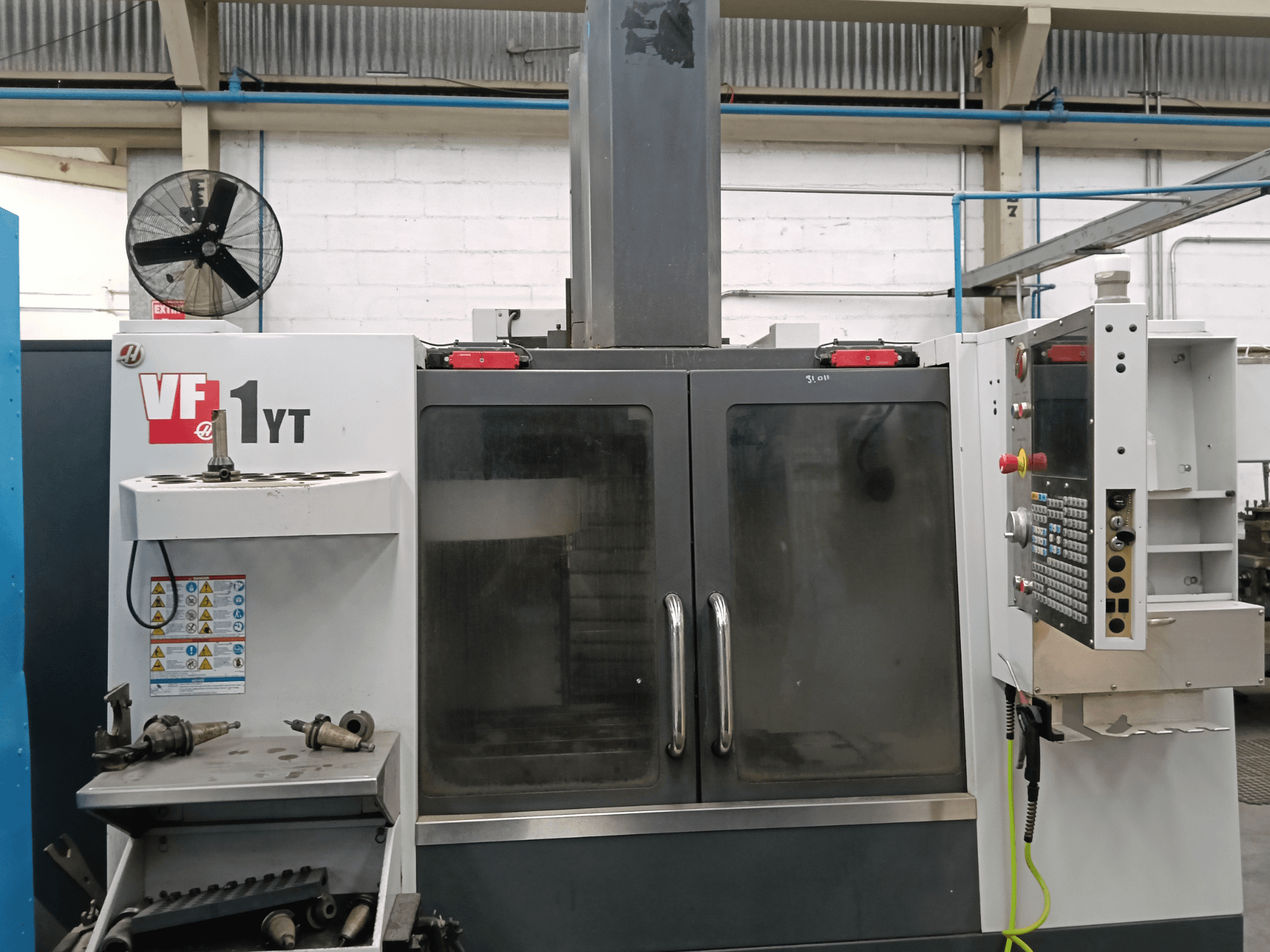 Вид спереди на вертикальный обрабатывающий центр HAAS VF-1YT-1 с панелью управления и инструментами сбоку.