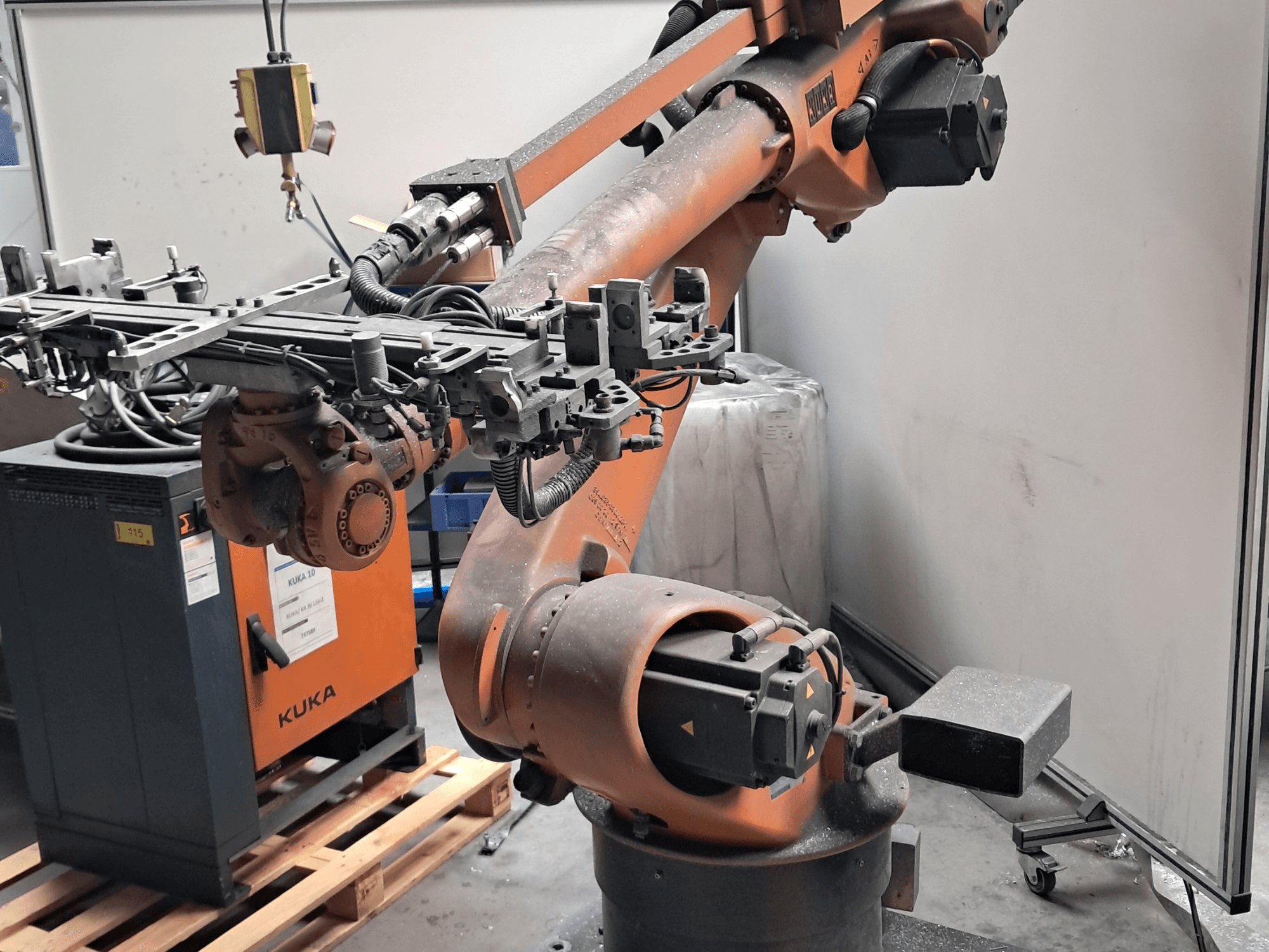 Манипулятор робота KUKA KR 30L16-2 в боковом ракурсе с сложным концевым эффектором и кабелями управления, расположенный рядом с блоком управления KUKA.