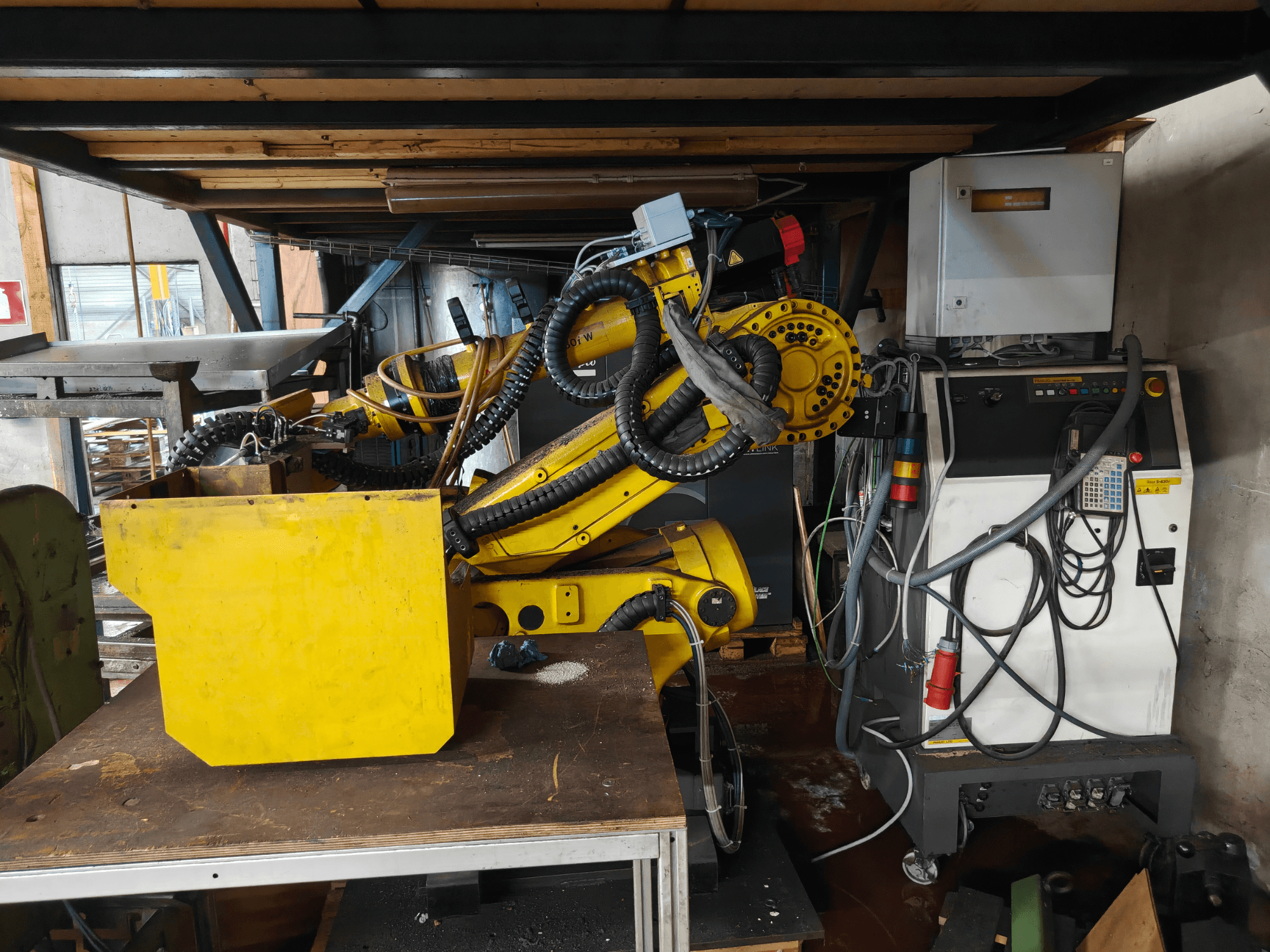 Вид спереди на манипулятор робота FANUC S-430i W желтого цвета с панелью управления, кабелями и желтым компонентом на рабочем столе.