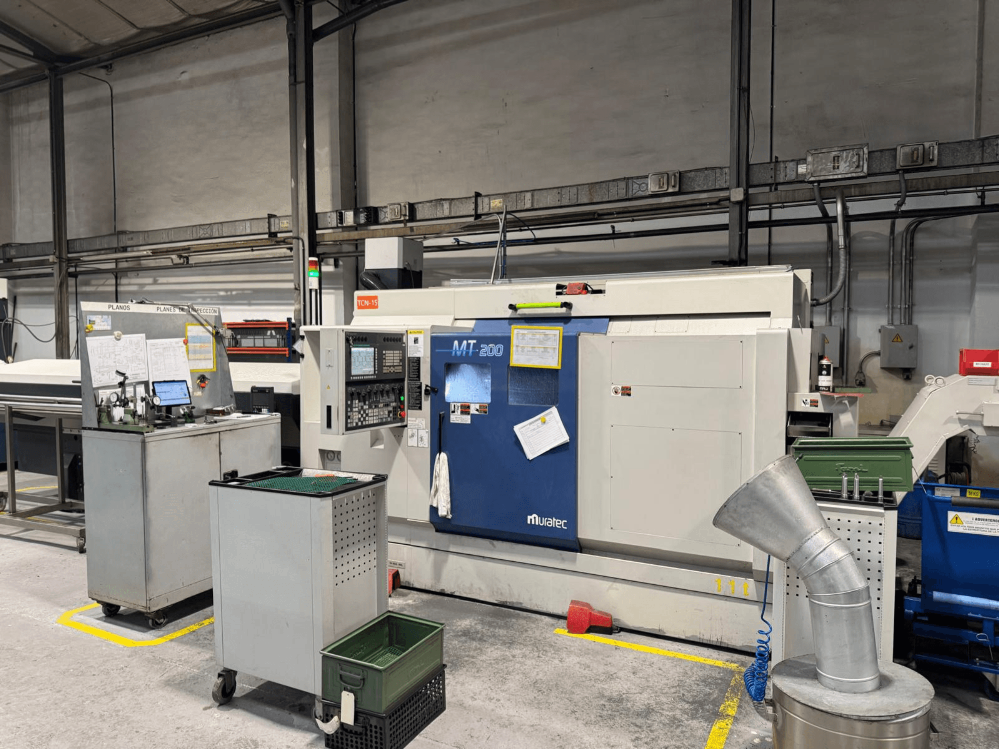 Многошпиндельный токарный станок Muratec MT200 в заводских условиях, вид спереди, с панелью управления и окружающим оборудованием.