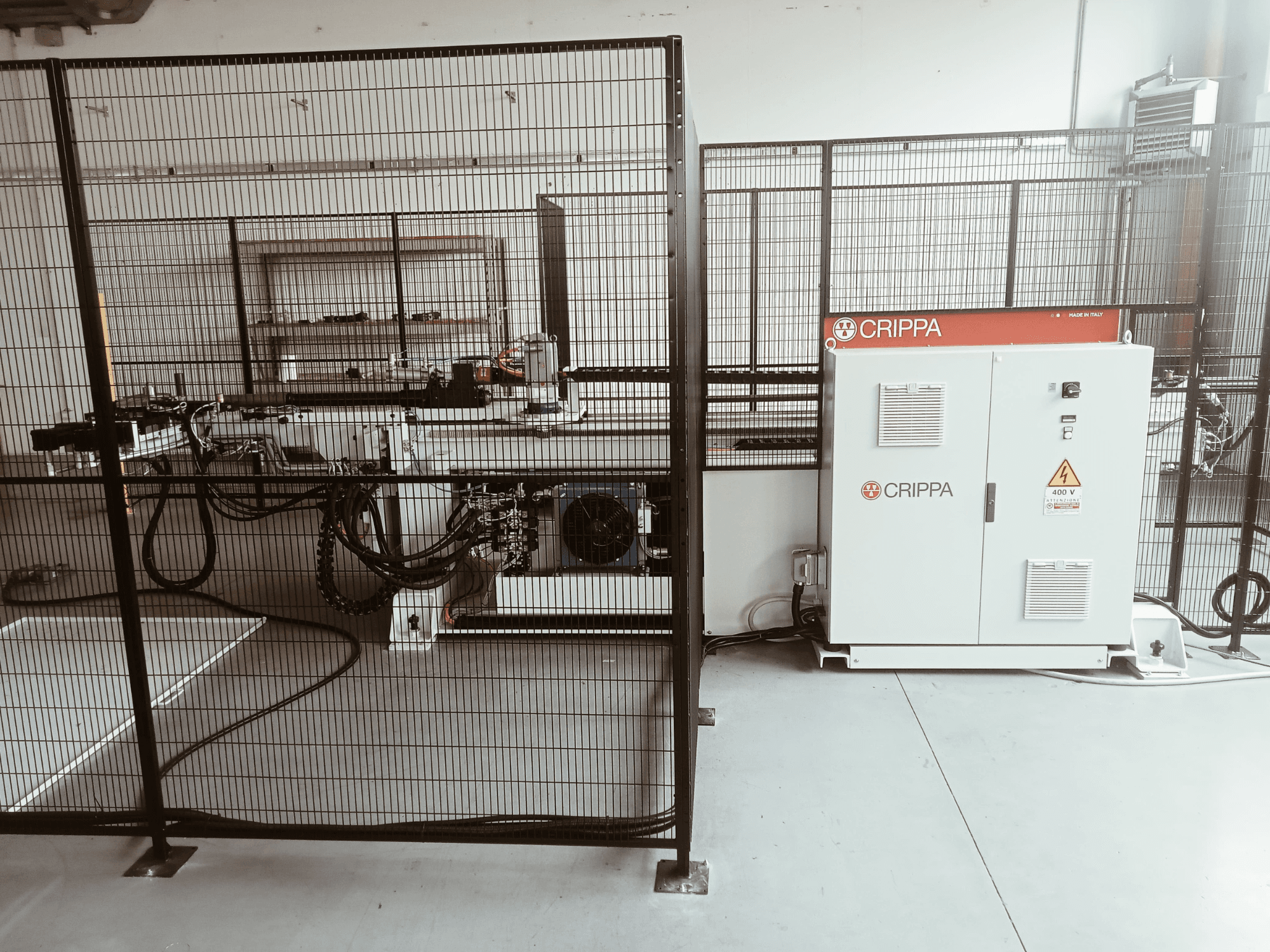 Белая машина CRIPPA за защитной клеткой, с видимыми шлангами и компонентами, вид сбоку, промышленная обстановка.