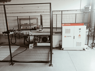 Белая машина CRIPPA за защитной клеткой, с видимыми шлангами и компонентами, вид сбоку, промышленная обстановка.