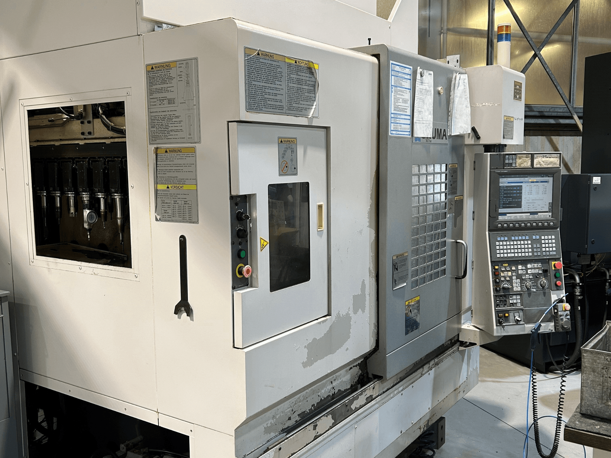 Вид спереди станка с ЧПУ UMA с видимыми держателями инструментов, панелью управления, предупреждающими надписями и кнопками управления.