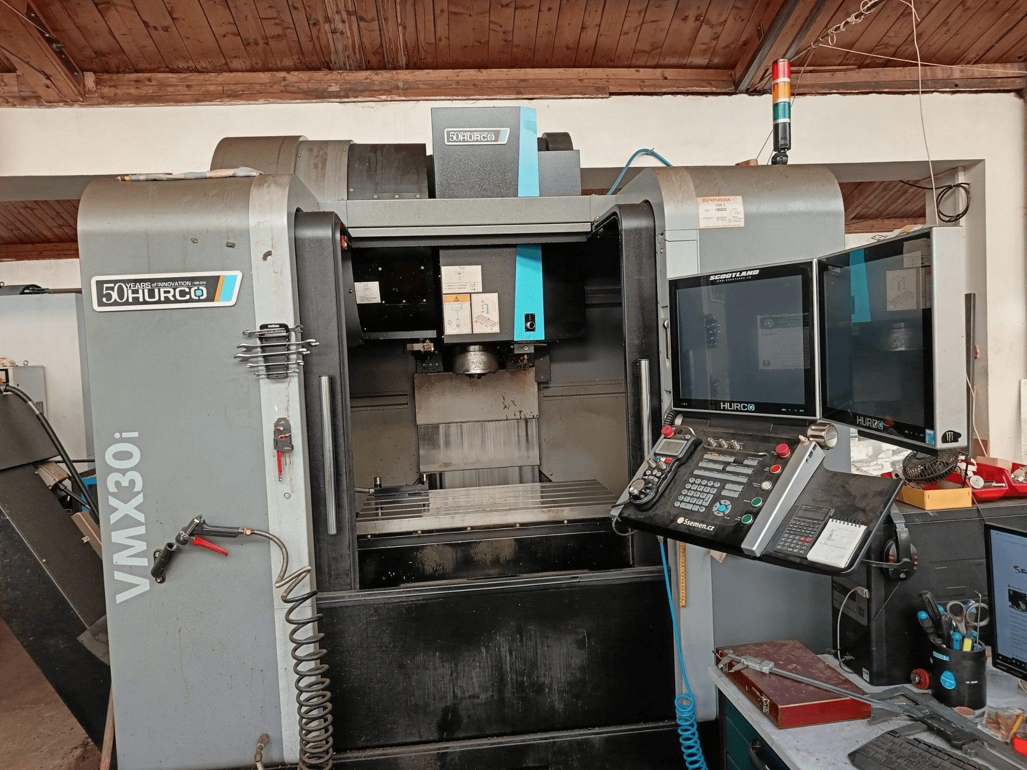 Фрезерный станок с ЧПУ Hurco VMX30i с видом спереди, с двумя мониторами, панелью управления и присоединенным шлангом.
