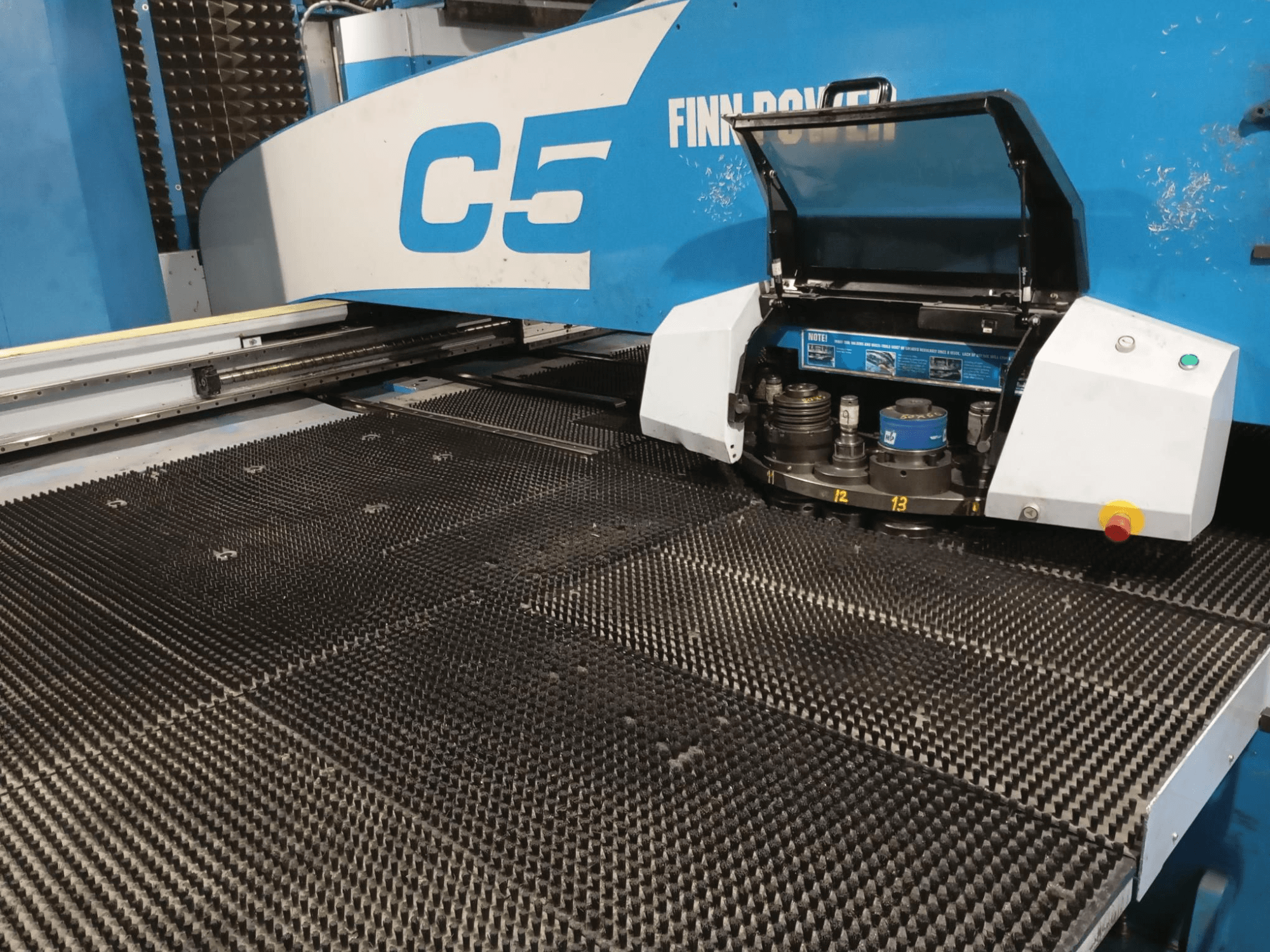 Пробивной пресс Finn-Power C5, вид спереди, видна открытая инструментальная головка над рабочим столом с текстурированной поверхностью и пронумерованными точками индексации.