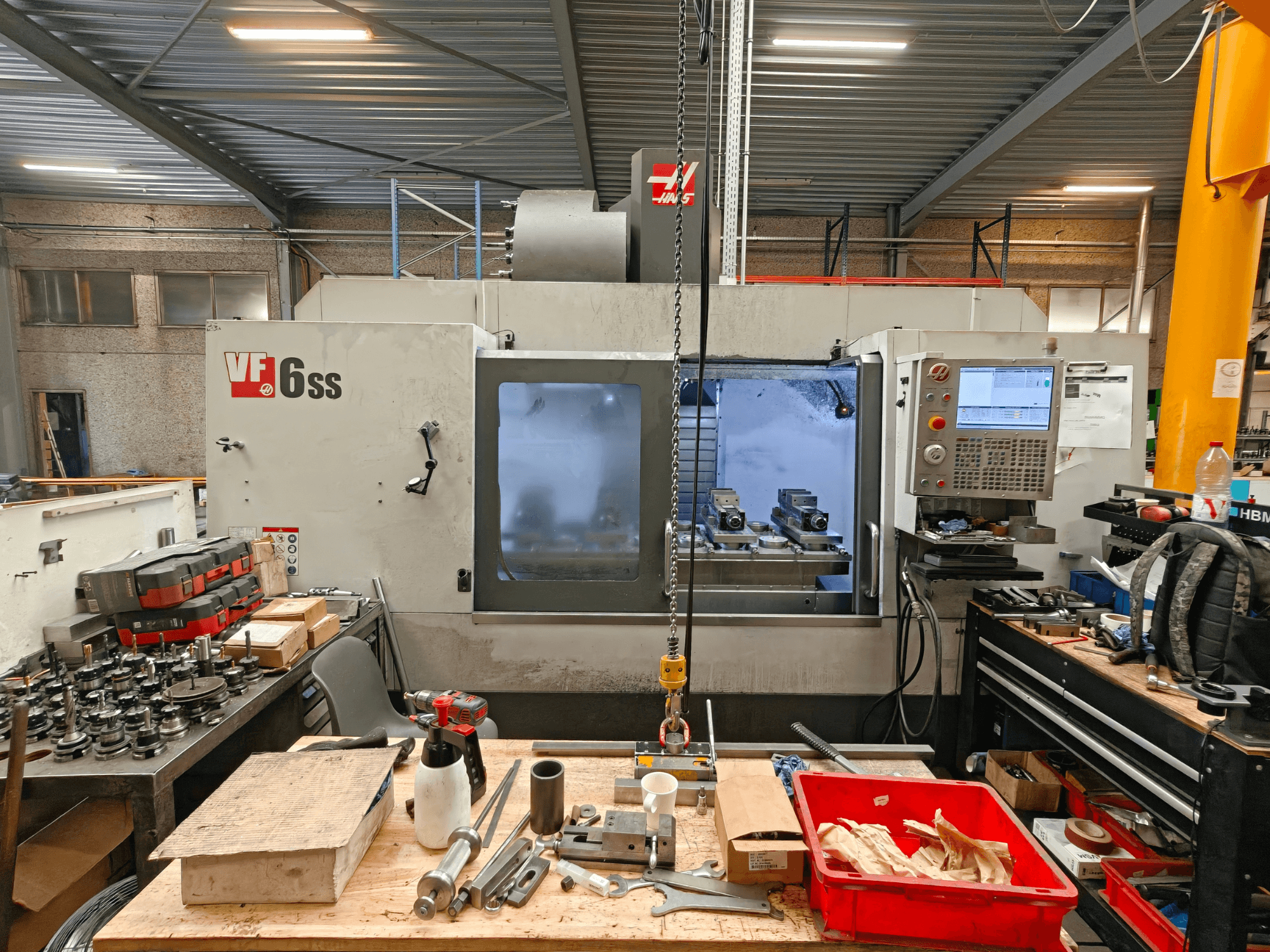 Вертикальный обрабатывающий центр Haas VF-6SS в цехе, вид сбоку, на котором видны панель управления и рабочая зона, заваленная инструментами.