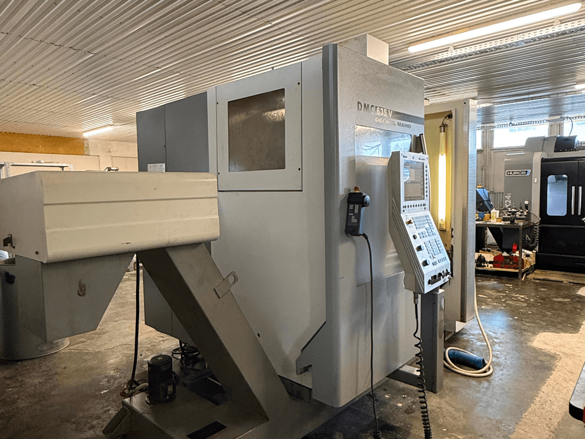 Фрезерный станок DMC G635V в мастерской, вид спереди, видна панель управления и подключенные электроинструменты.