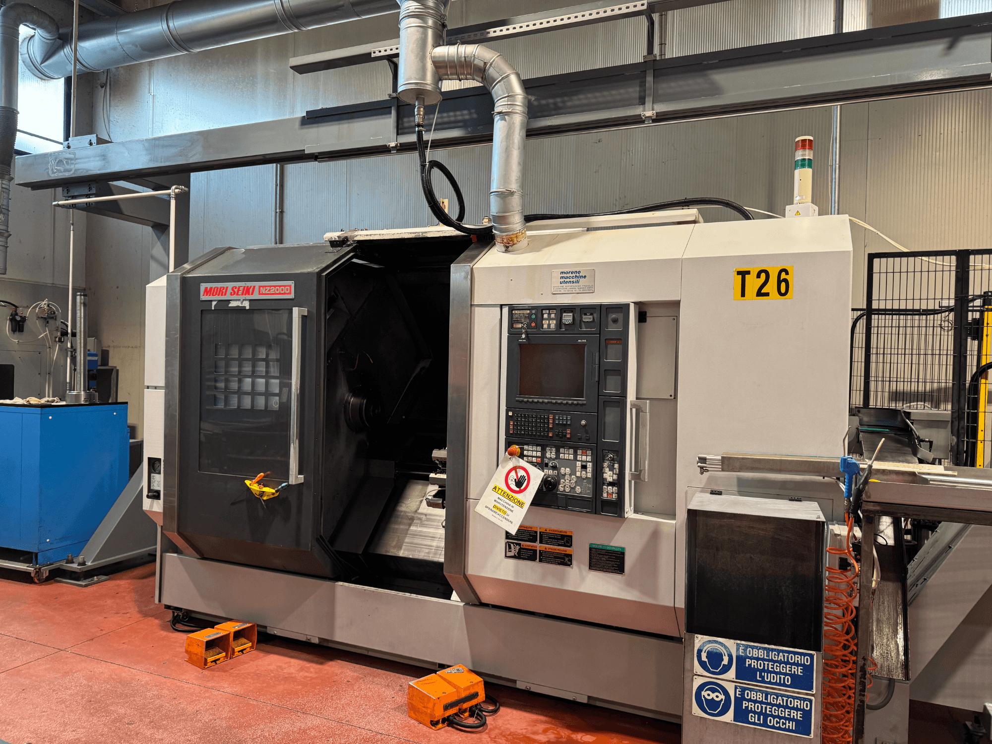 Токарно-фрезерный центр MORI SEIKI NZ-2000/T2/Y2, вид спереди, панель управления, знаки безопасности и промышленная установка.