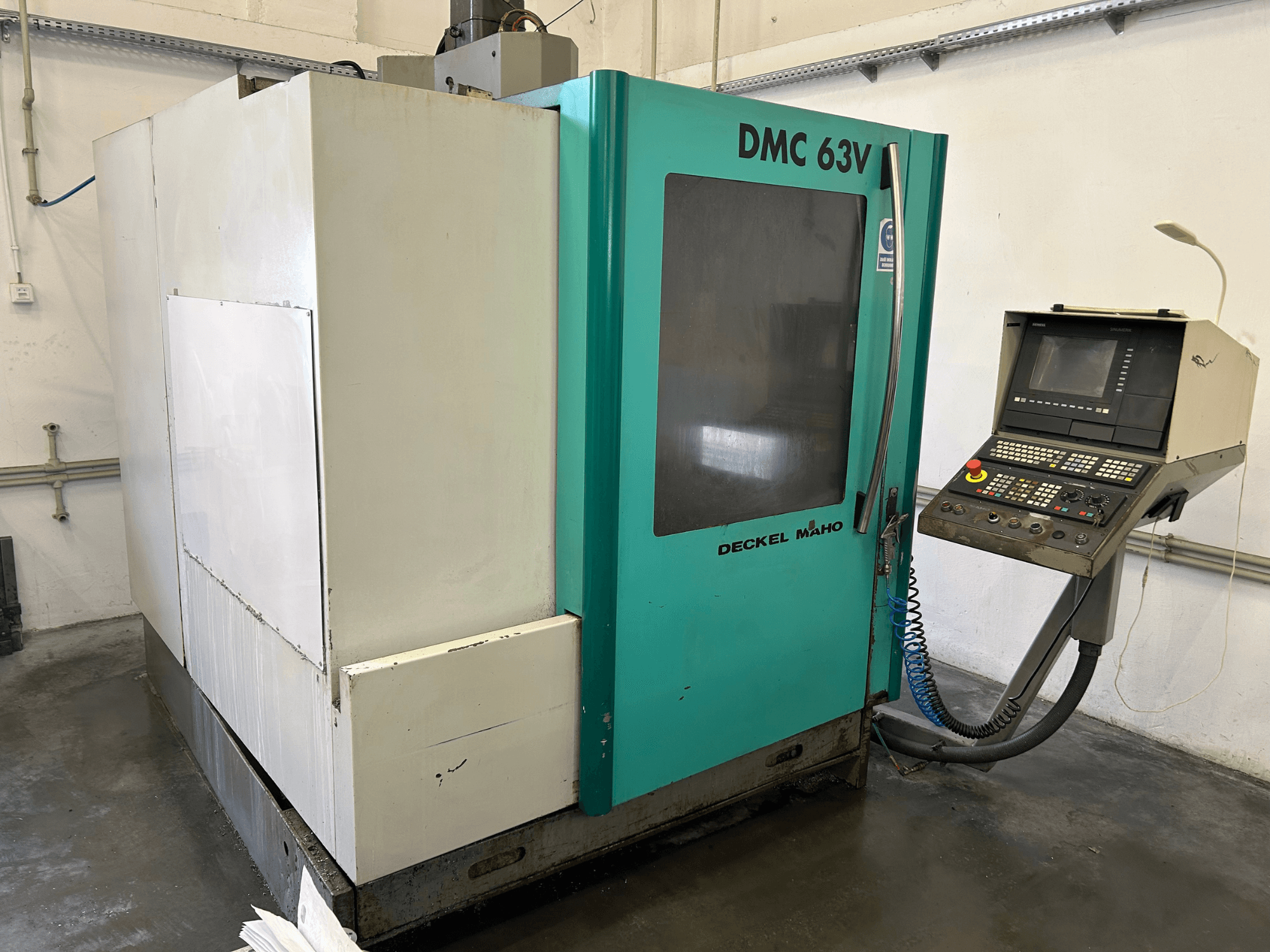 Вертикальный обрабатывающий центр DECKEL MAHO DMC 63V на виде спереди, с панелью управления и в сине-зеленом корпусе.