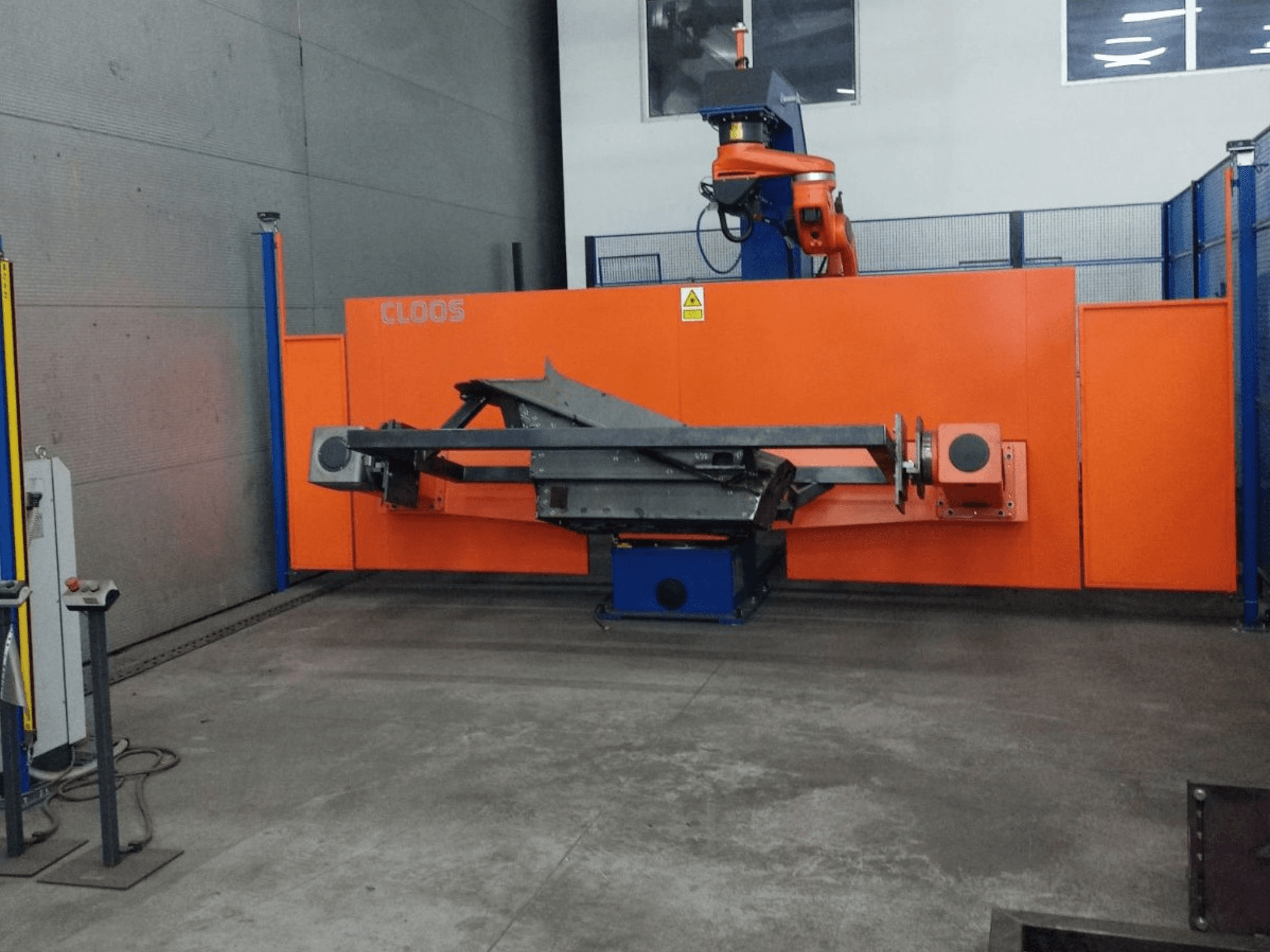Вид спереди на систему автоматизации CLOOS QIROX QRC-350-E с роботизированной рукой и металлоконструкцией в промышленных условиях.