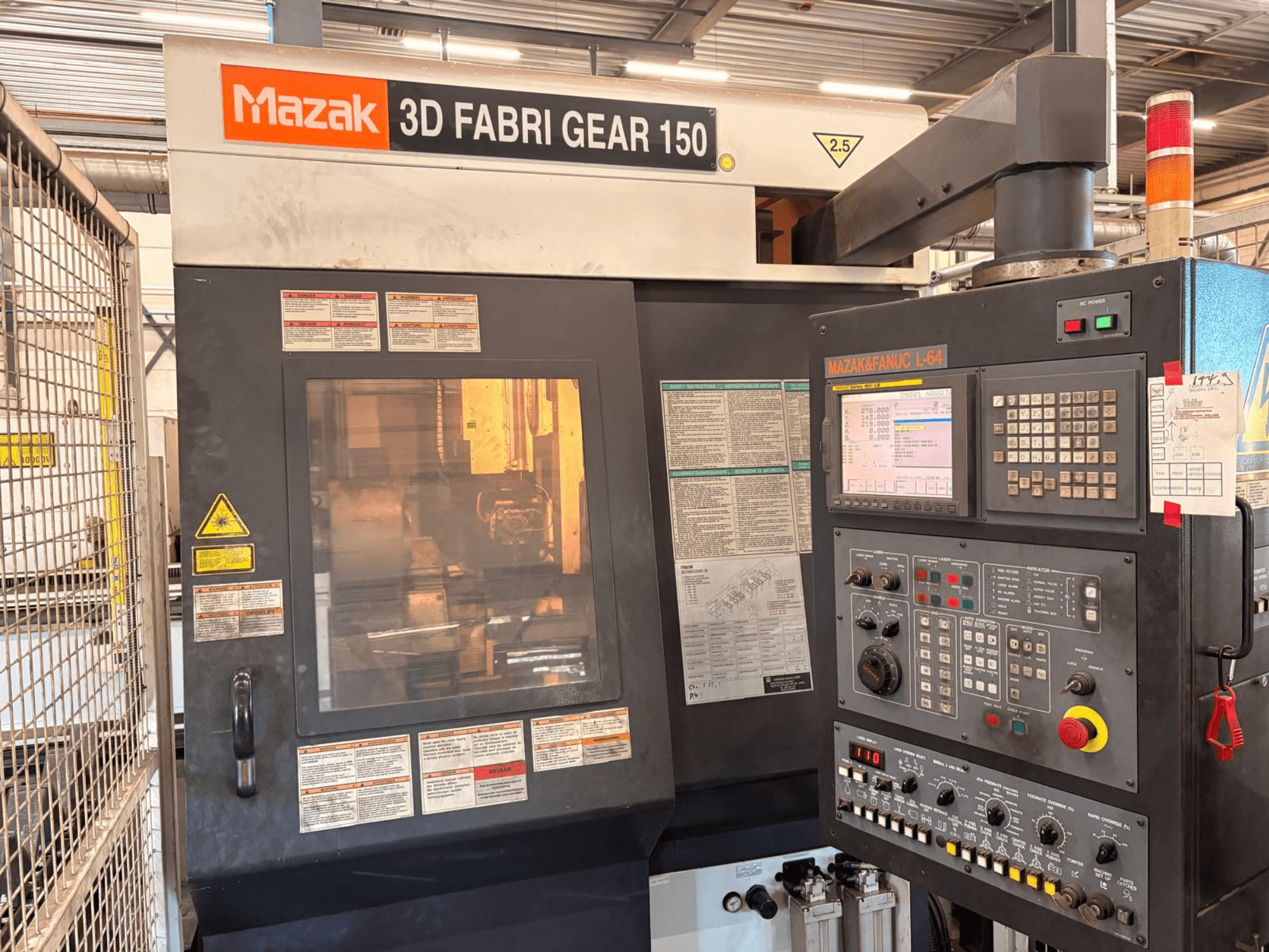 Станок для резки труб Mazak 3D Fabri Gear 150, вид спереди с панелью управления, предупреждающими надписями и рабочим интерфейсом.