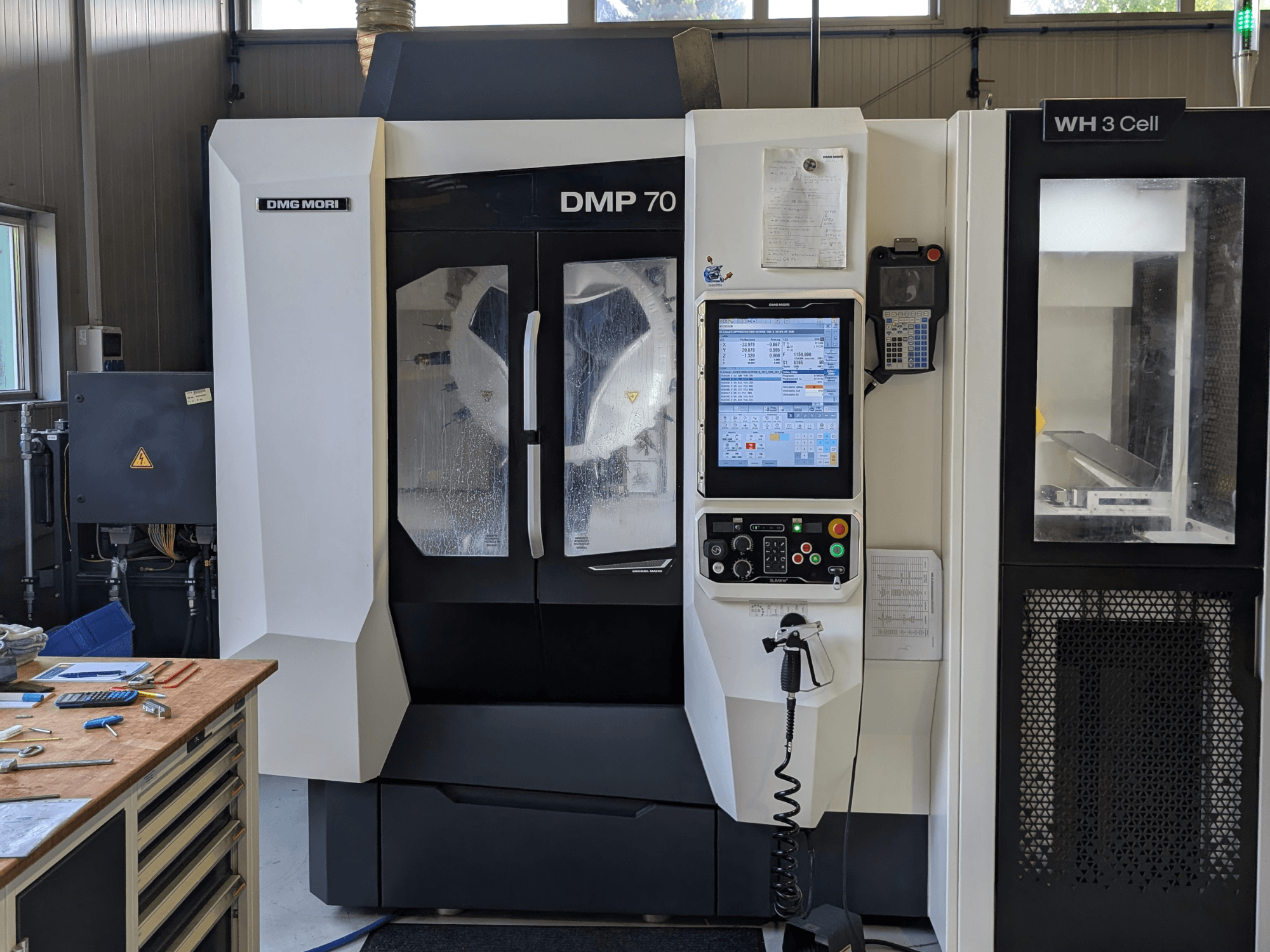 Вертикальный обрабатывающий центр DMG MORI DMP 70, вид спереди с панелью управления и рабочим дисплеем, в окружении слесарных инструментов.