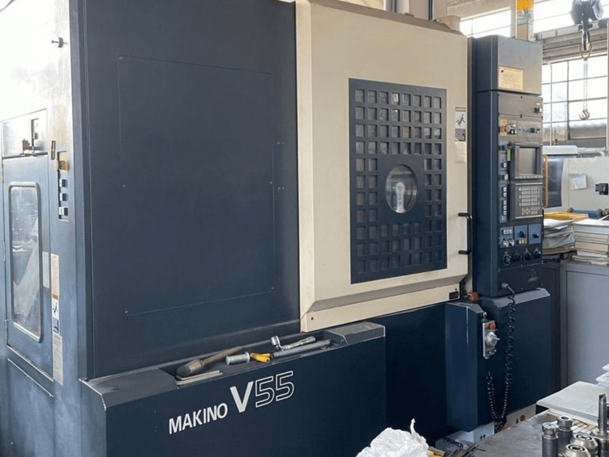 Вертикальный обрабатывающий центр Makino V55-A15, вид спереди с панелью управления, прочной конструкцией и конфигурацией рабочей зоны.