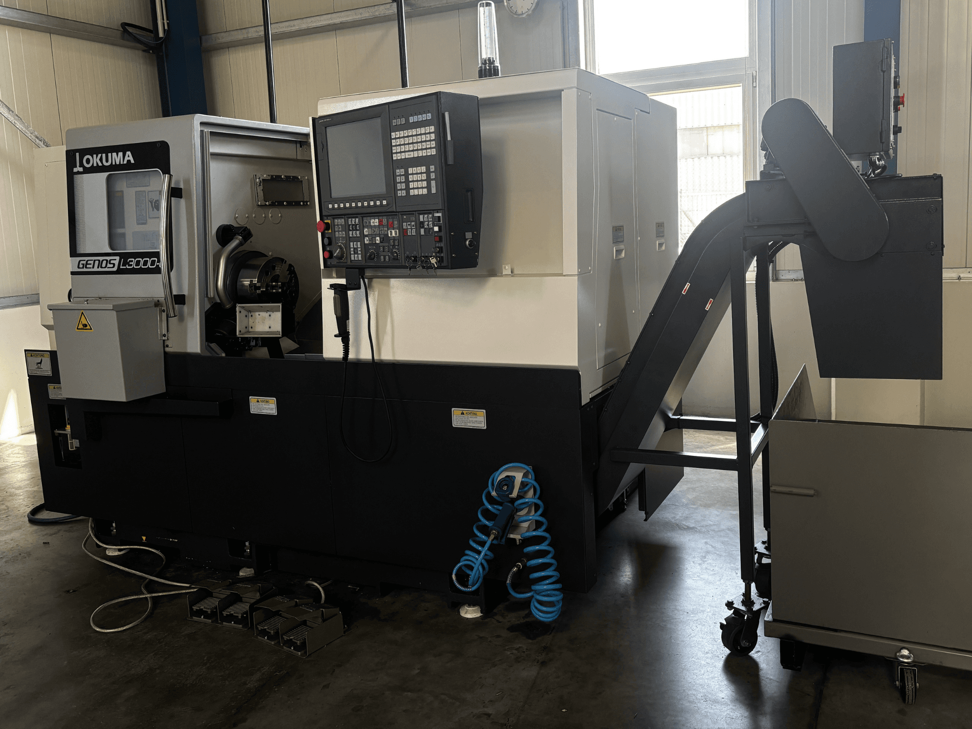 Горизонтальный токарный станок Okuma GENOS L3000-e, вид спереди: на фотографии видны панель управления, конвейер и область шпинделя.