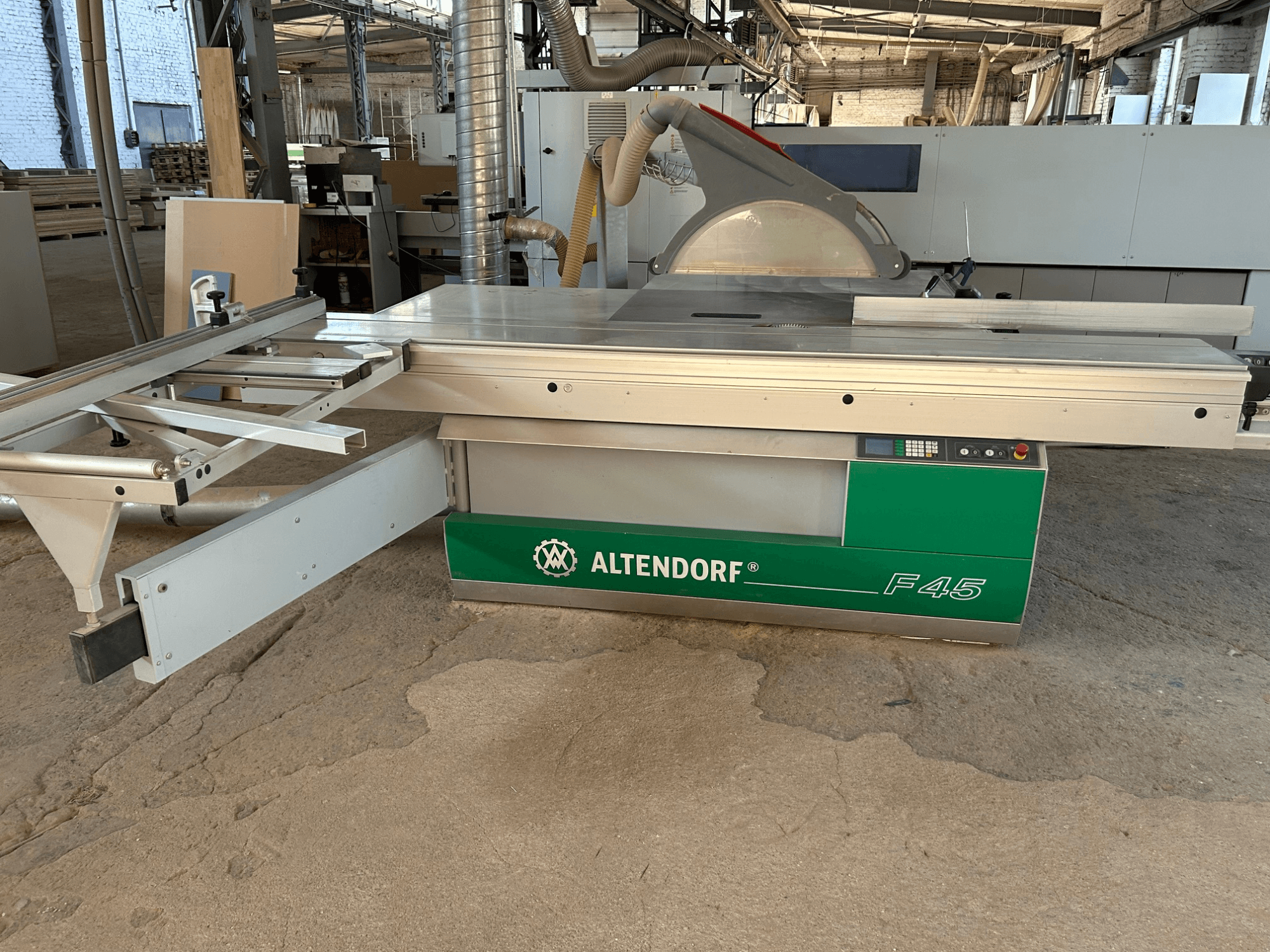 Пила для распиловки плит Altendorf F 45, вид спереди, на котором видны рабочий стол, кожух пильного диска и панель управления на станке зелёно-серого цвета.