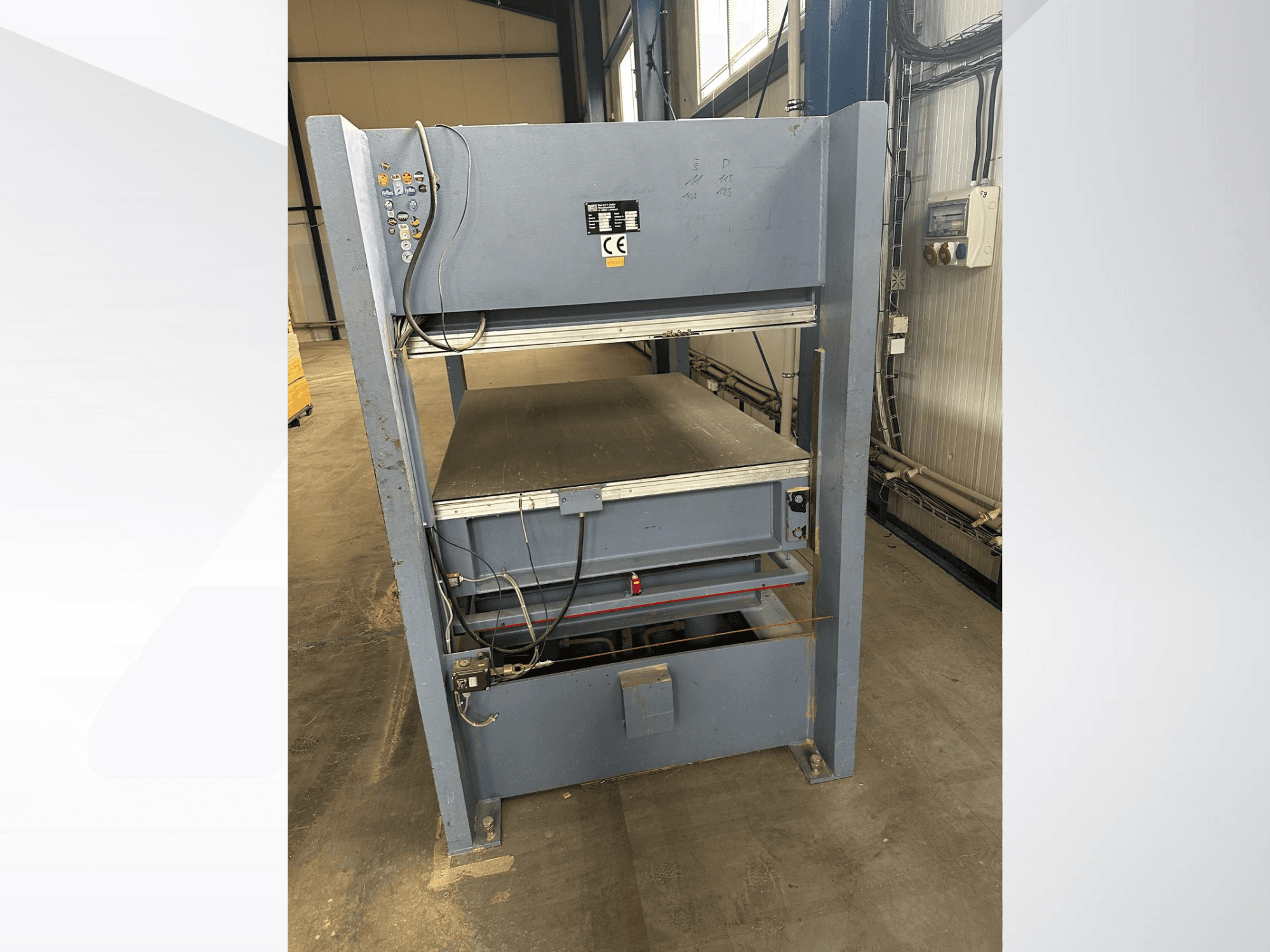 Серый промышленный станок с панелью управления, вид спереди; включает регулируемые платформы и знаки безопасности.