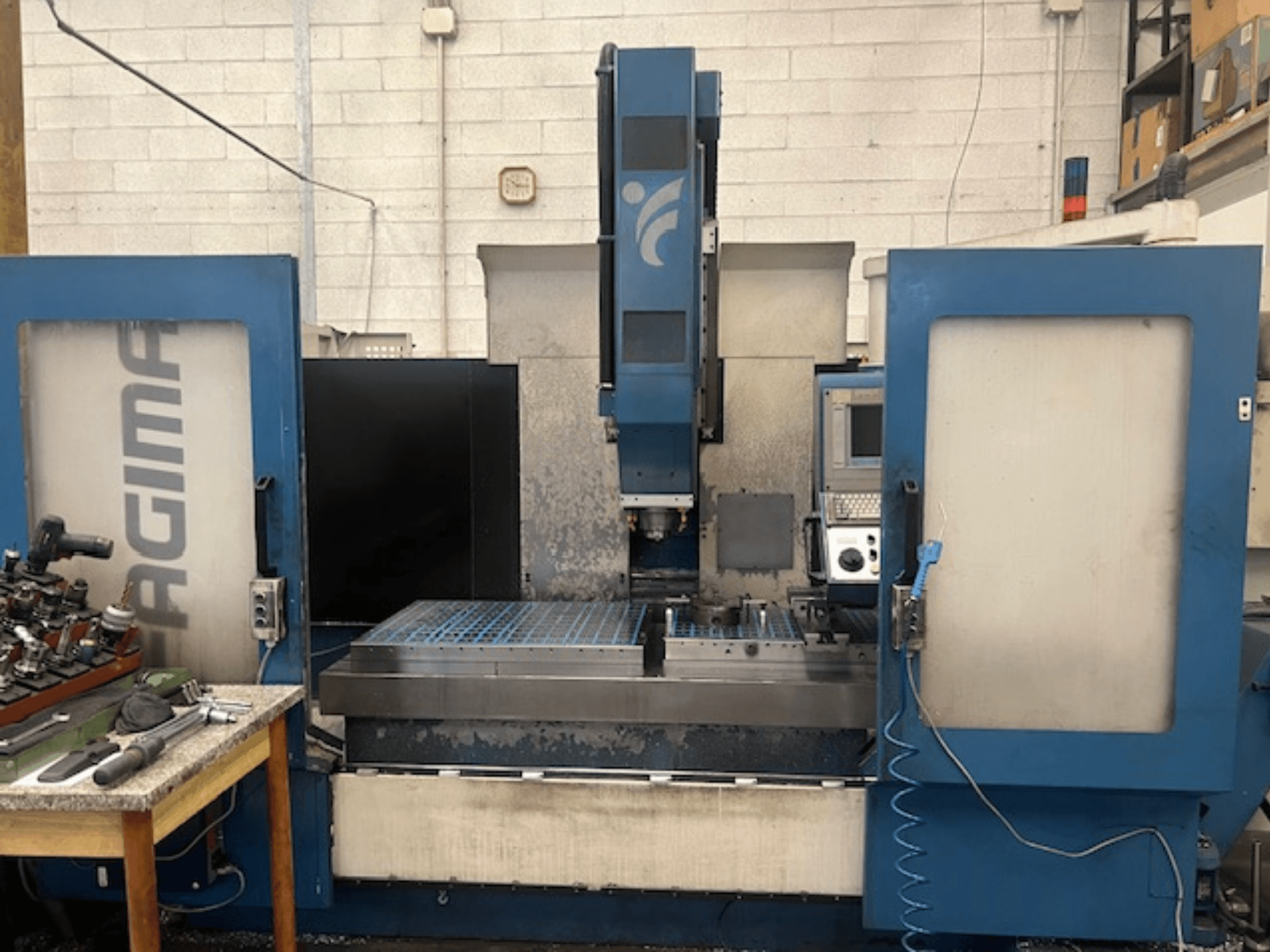 Вид спереди на станок с ЧПУ JAGIMA с большой металлической рабочей зоной, видимой панелью управления и инструментами на соседнем столе.