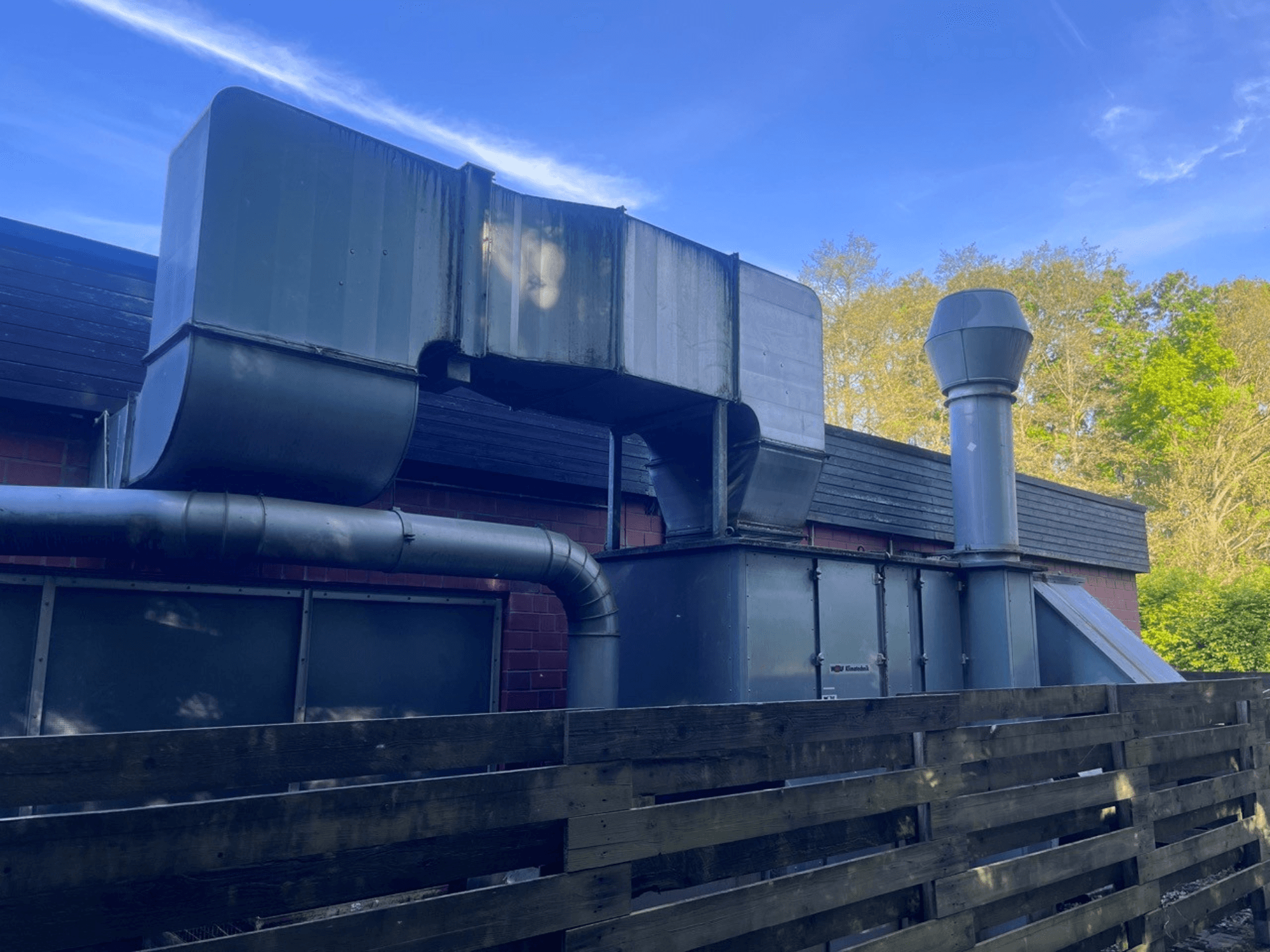 Промышленная вентиляционная система с металлическими воздуховодами, вид сбоку; включает квадратную и цилиндрическую дымовую трубу, отделка зеленого цвета.