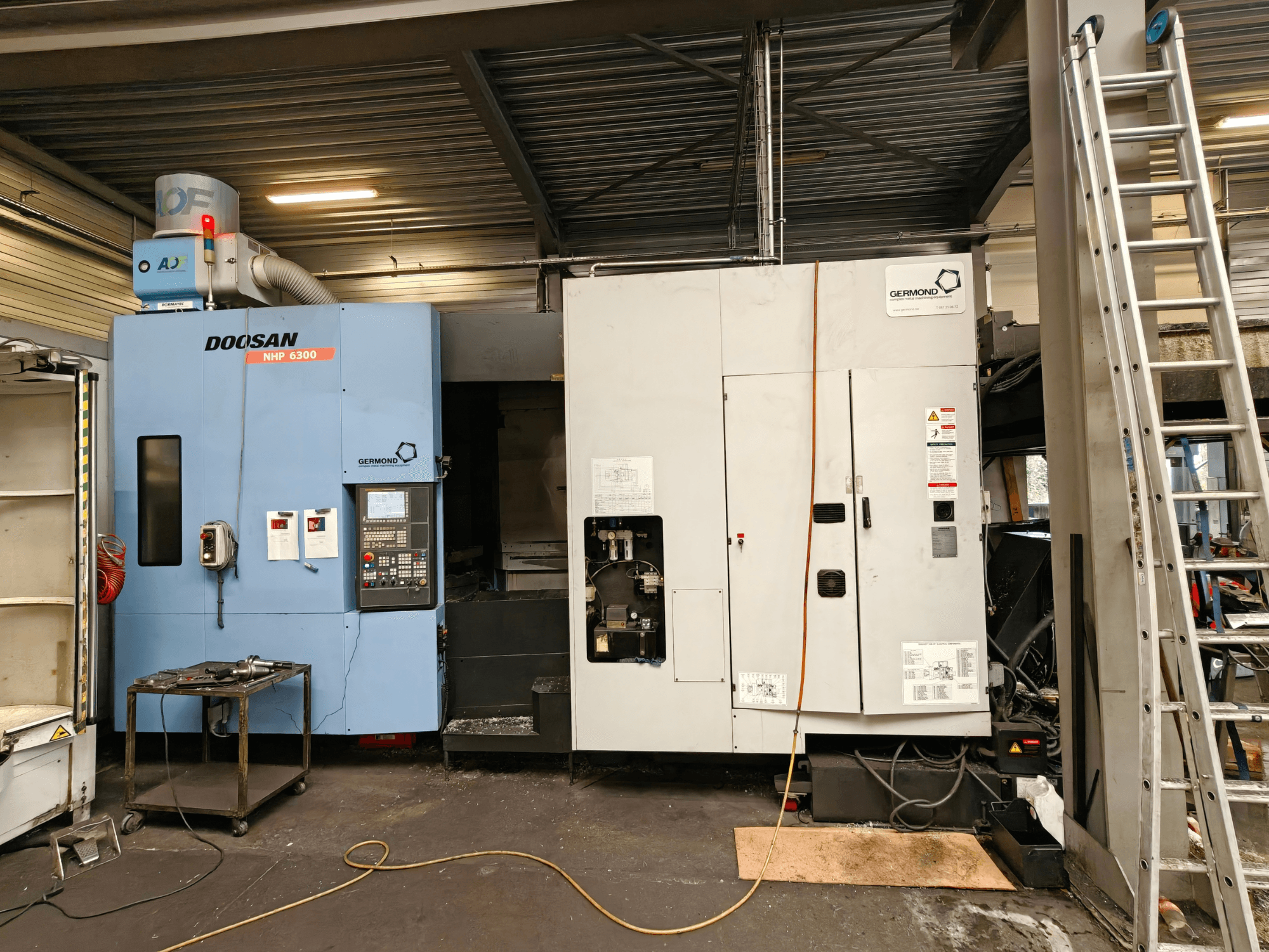 Горизонтальный обрабатывающий центр DOOSAN NHP6300 в виде спереди, на котором видны панель управления и соседнее оборудование в условиях цеха.