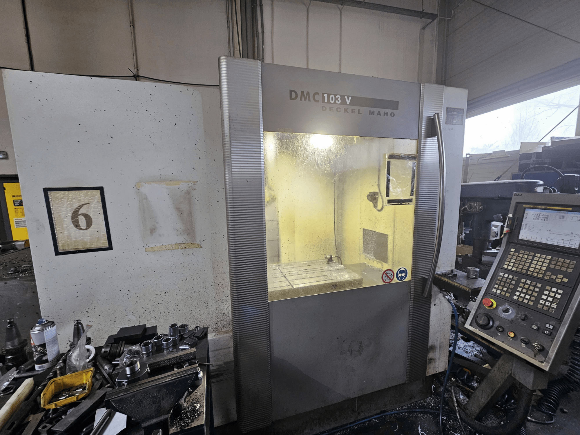 Вид спереди станка с ЧПУ Deckel Maho DMC 103 V, на котором видны панель управления, рабочая зона и нумерованный индикатор "6".