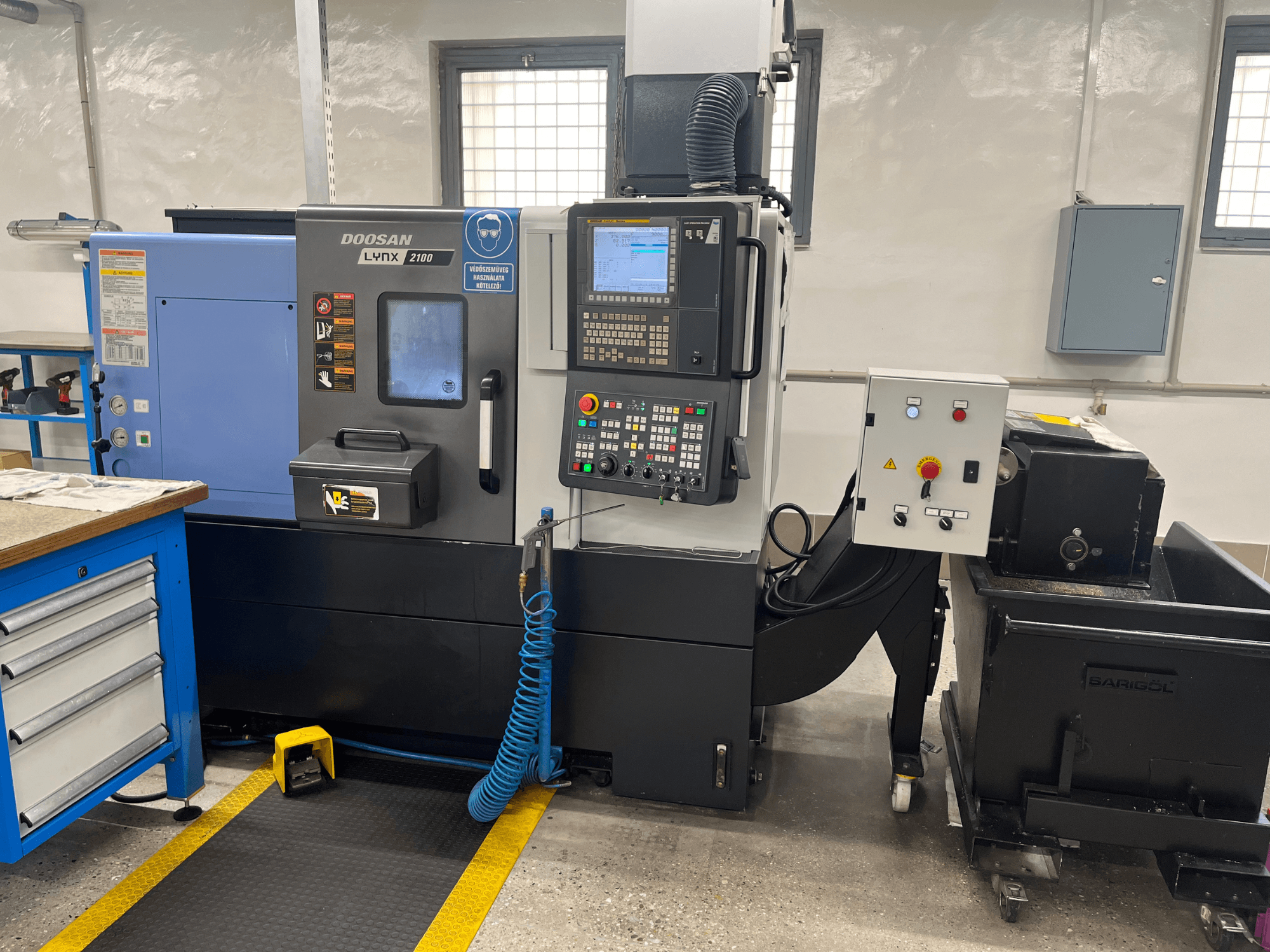 Токарный станок Doosan Lynx 210 в мастерской, панель управления, хранилище инструментов и система охлаждения, вид сбоку с деталями рабочего пространства.