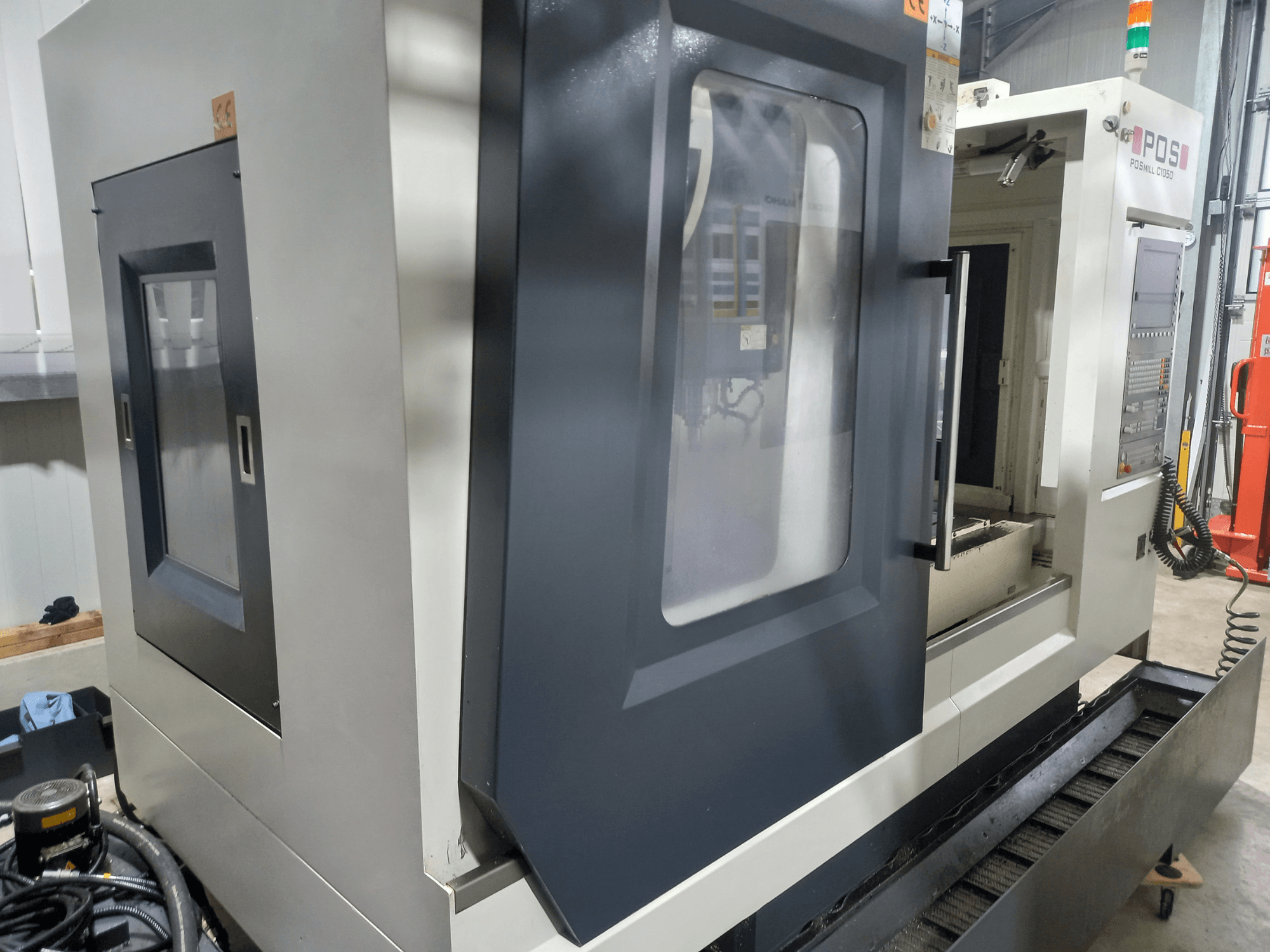 Вертикальный обрабатывающий центр POSmill C 1050, вид сбоку с открытой дверцей, на котором видны рабочая зона и детали панели управления.