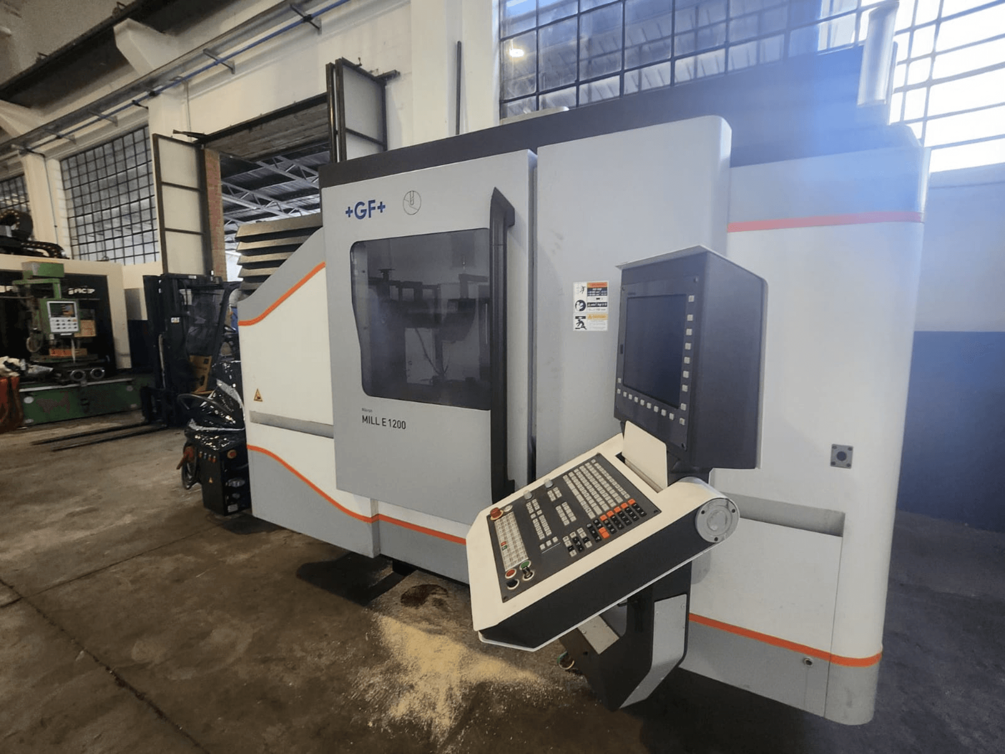GF MILL E1200, вид спереди фрезерного станка с панелью управления, экраном и наклейками безопасности, в мастерской.