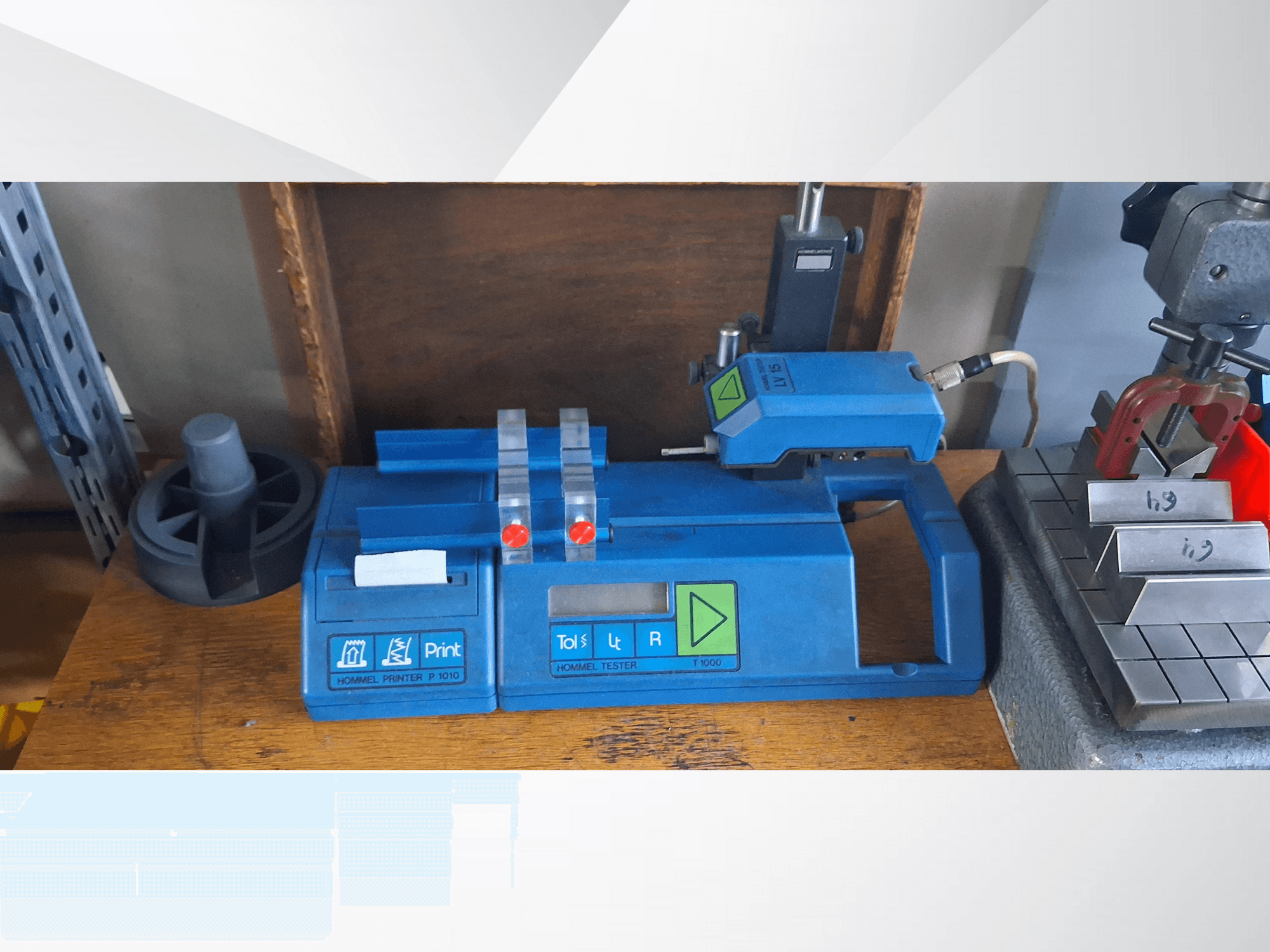 Синий принтер Hommel T 1000 и тестер T 1 010 с красными кнопками, вид спереди на верстаке с металлическими блоками.