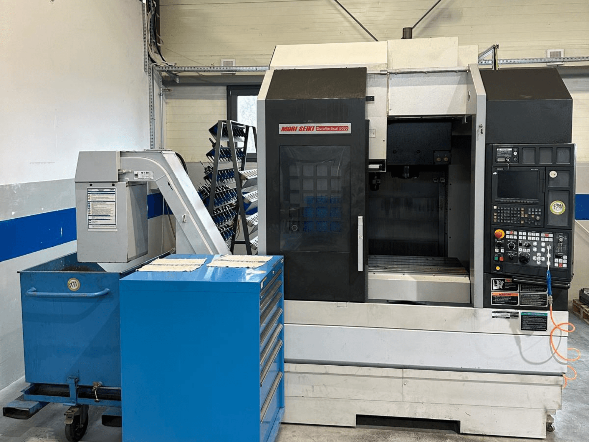 MORI SEIKI DURA VERTICAL 5060 — вид спереди на вертикальный обрабатывающий центр с панелью управления и расположенным рядом хранилищем инструментов.