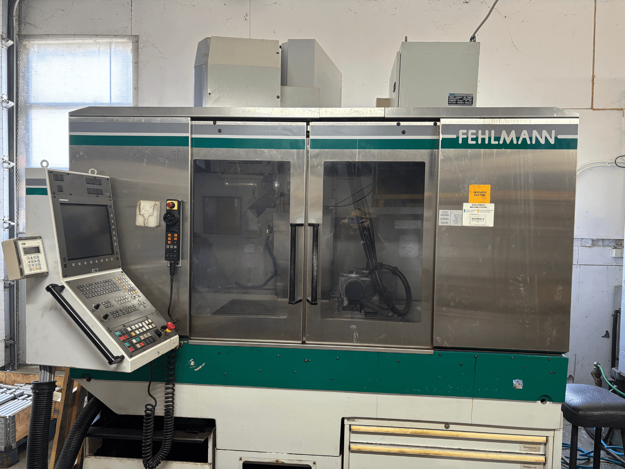 Вид спереди на вертикальный обрабатывающий центр FEHLMANN Picomax 90-M с панелью управления, прозрачным кожухом и кнопками управления.