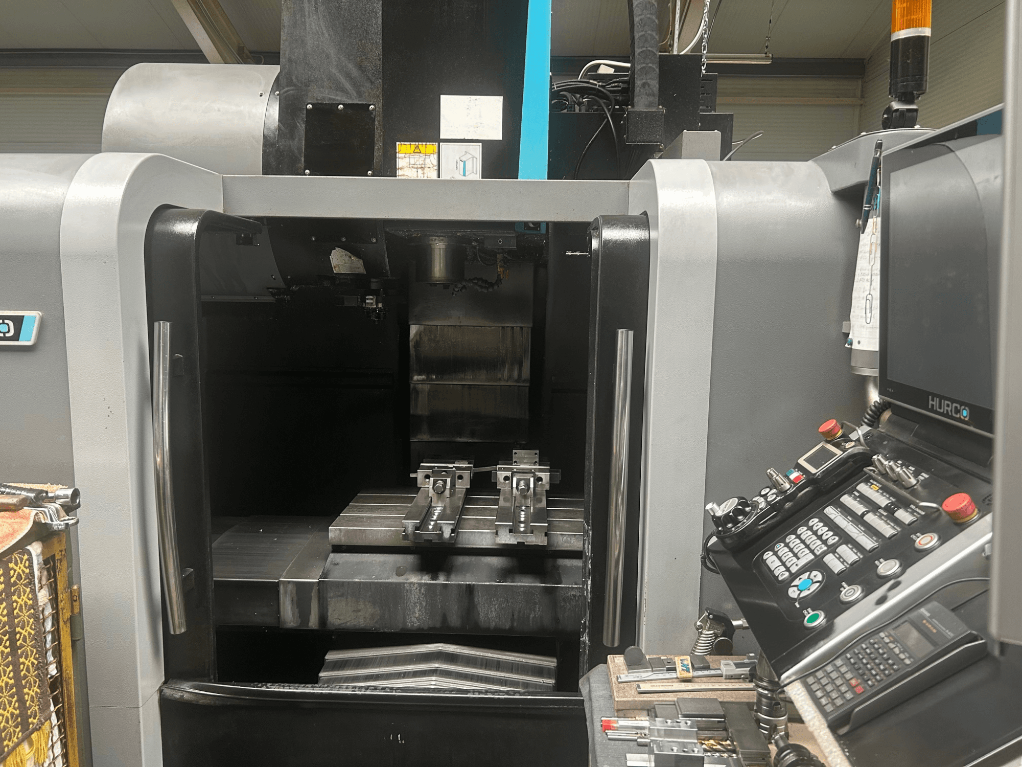 Вид спереди на обрабатывающий центр с ЧПУ Hurco, где показаны держатель инструмента, металлическая заготовка и панель управления с кнопками и дисплеем.