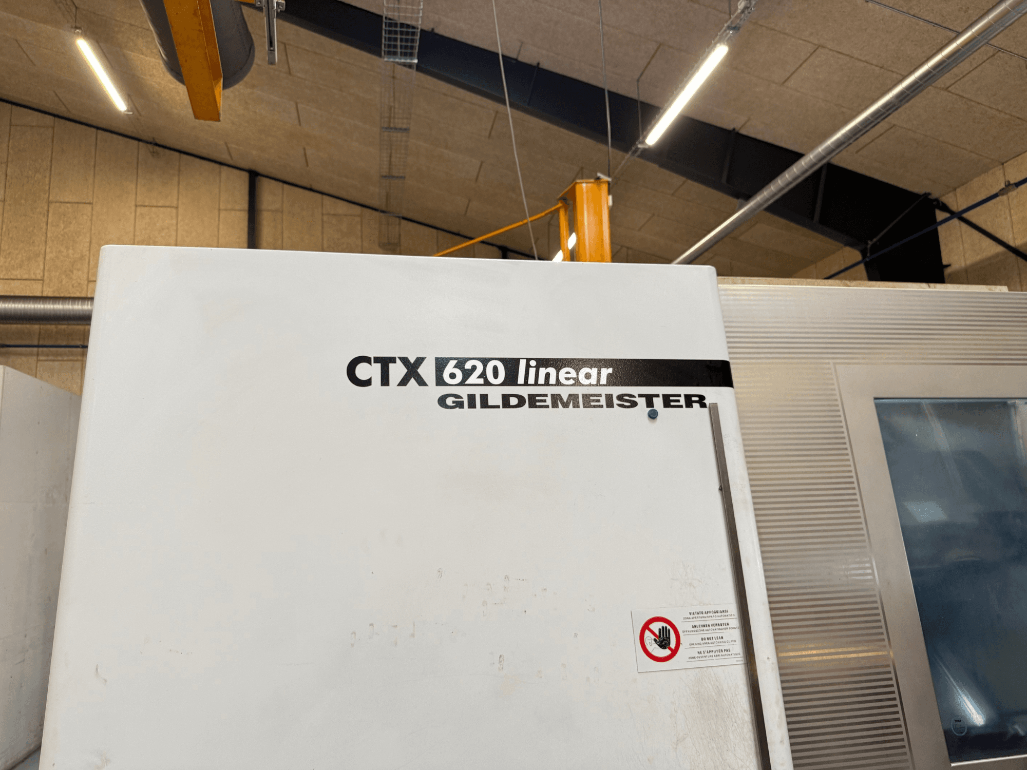 Вид сбоку машины CTX 620 Linear Gildemeister с белой внешней стороной и предупреждающими надписями.