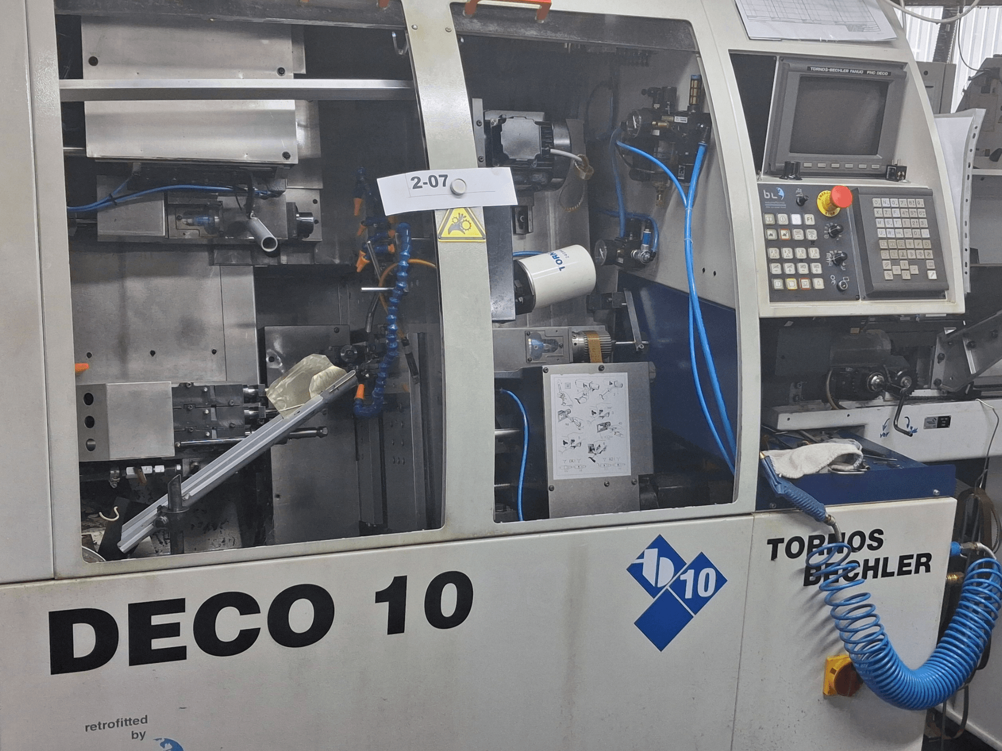 Токарный станок швейцарского типа TORNOS Deco 10a крупным планом, демонстрирующий внутренний механизм и детали панели управления.