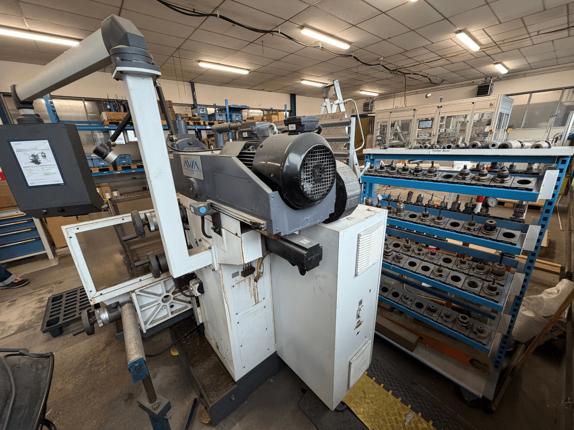 Универсальный обрабатывающий центр Avia FNX30NC, вид спереди с изображением панели управления и зоны хранения инструментов, на заднем плане — компоненты.