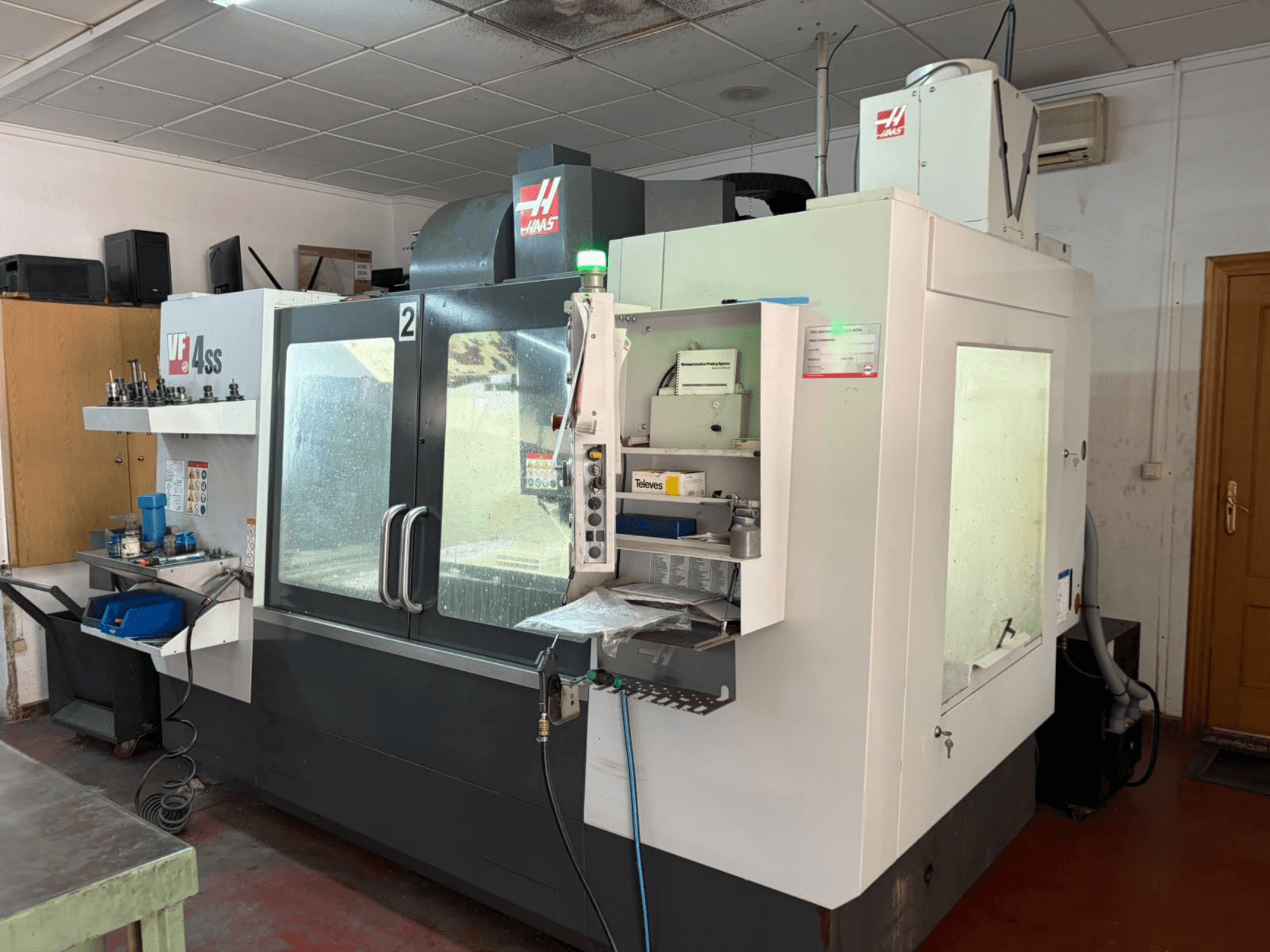 Вертикальный обрабатывающий центр HAAS VF 4SS в цехе, вид спереди, на котором видны панель управления и рабочая зона с инструментами и материалами.