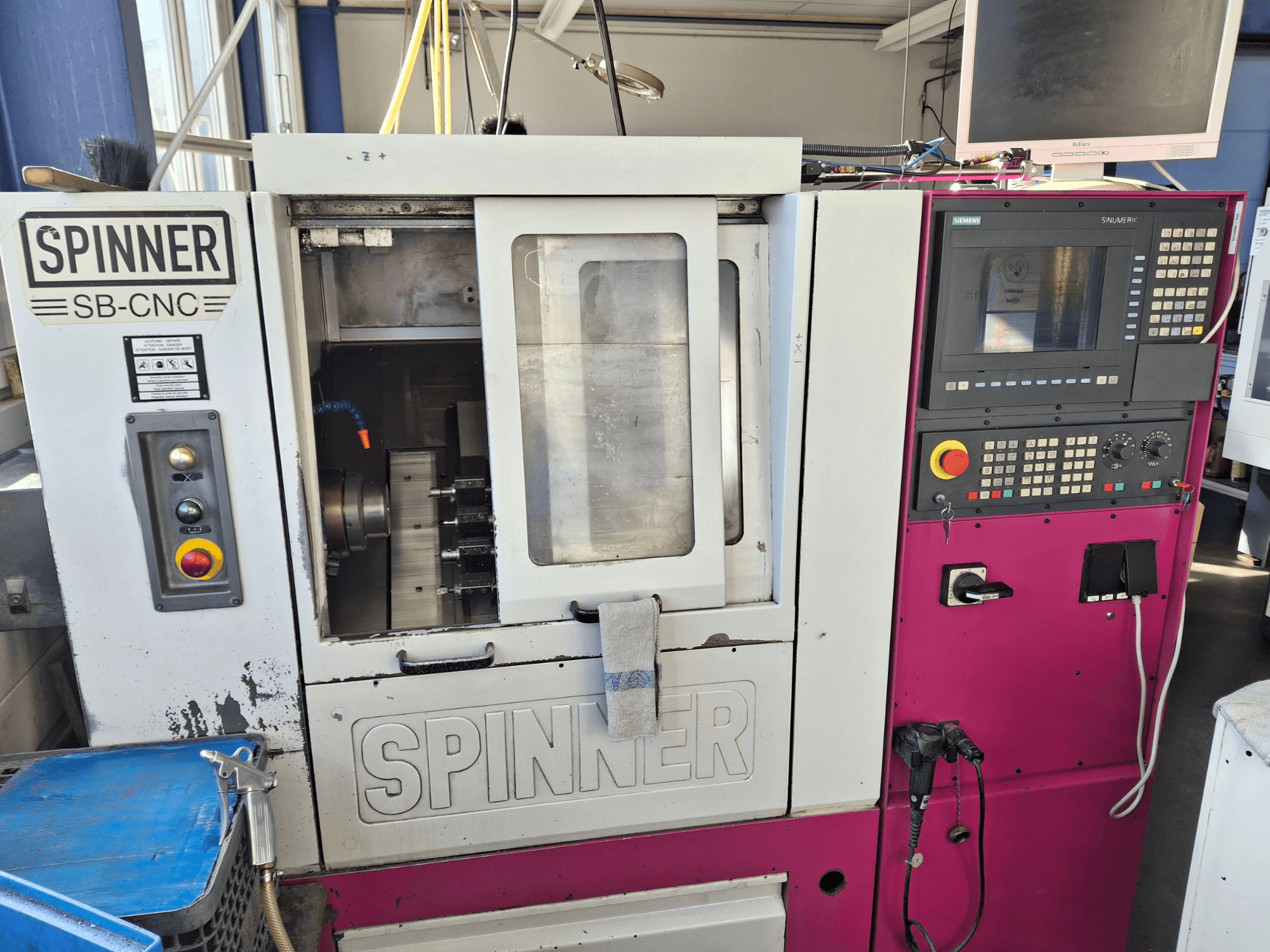 Горизонтальный токарный станок SPINNER SB-CNC, вид спереди с изображением панели управления, держателя инструмента и индикаторов работы.