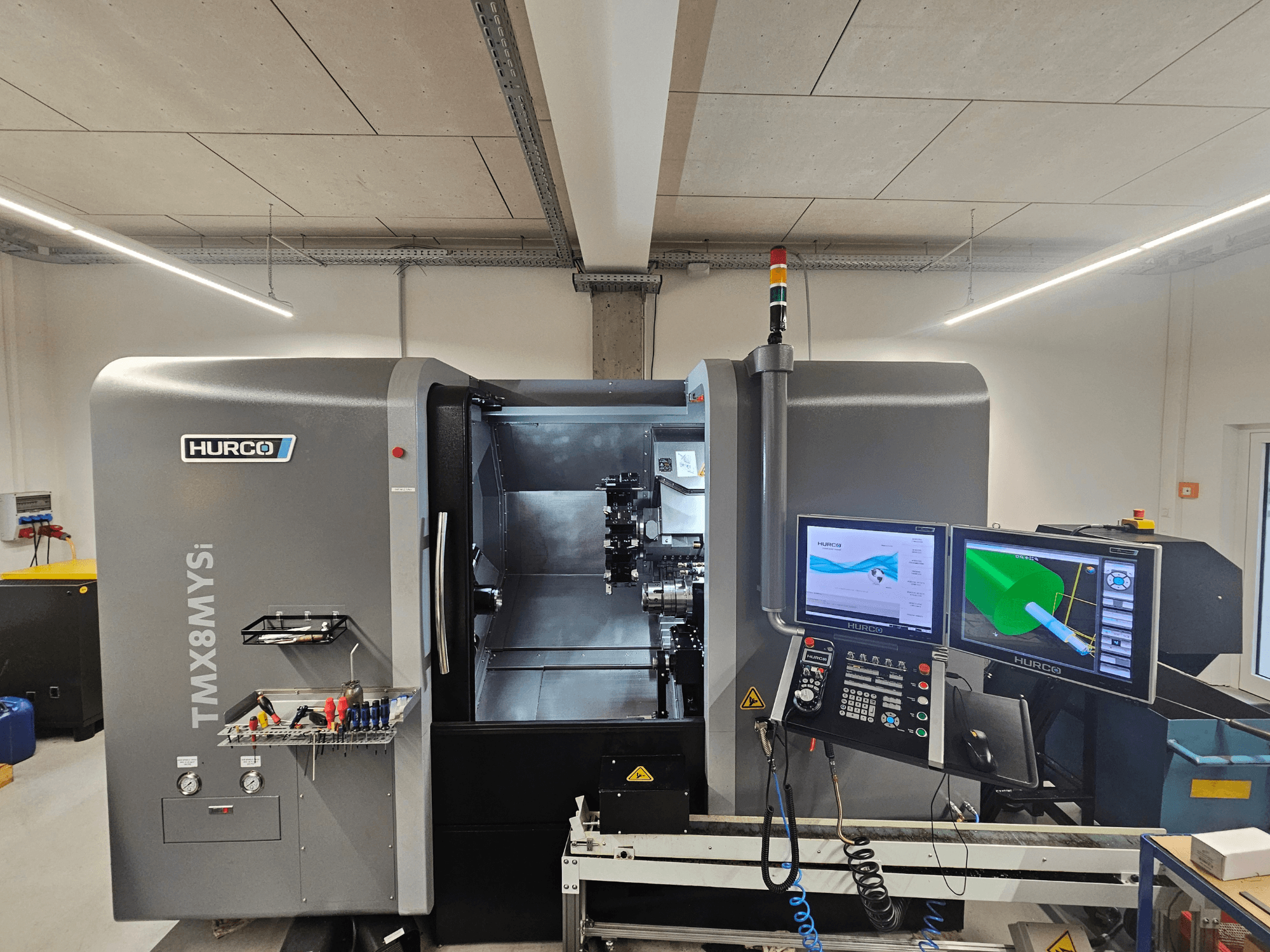 Токарно-фрезерный центр Hurco TMX 8 MYSi в мастерской, с двумя мониторами, панелью управления и инструментами сбоку.