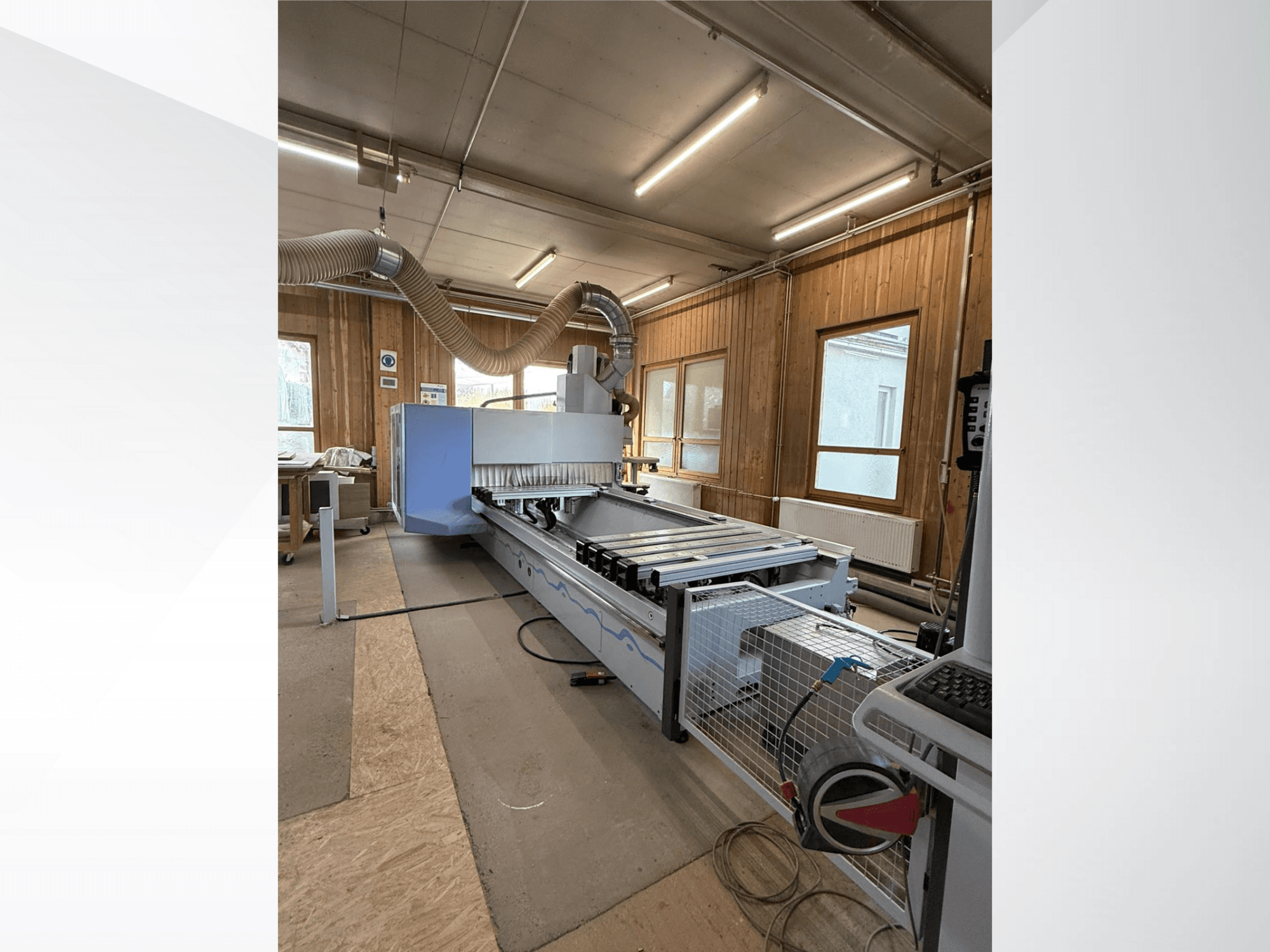 Фрезерный станок с ЧПУ в мастерской, вид сбоку, с большим синим корпусом, прикрепленным ленточным конвейером и видимой панелью управления.