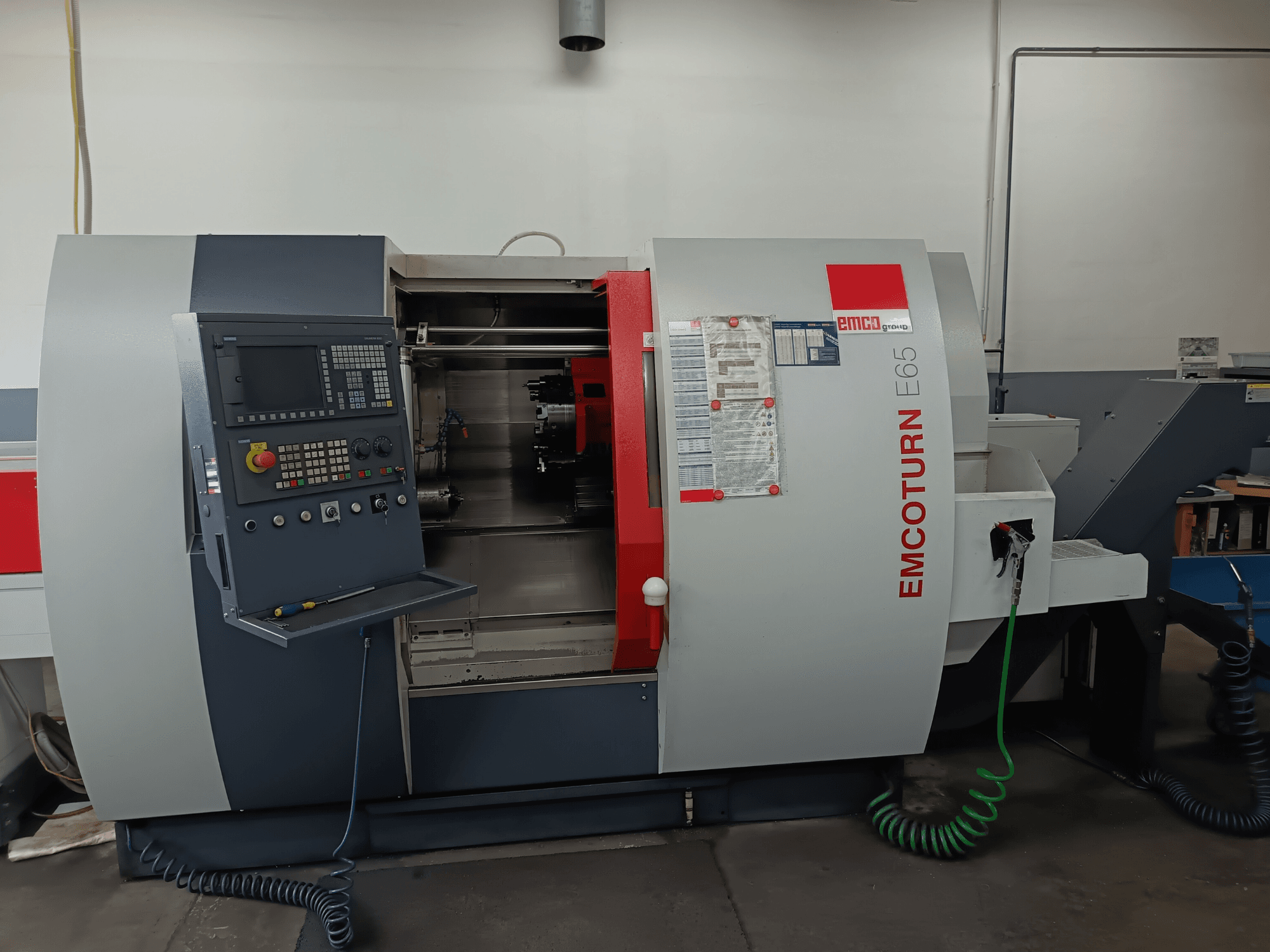Токарно-фрезерный центр EMCO EMCOTURN E65, вид спереди, демонстрирующий панель управления, внутренний механизм и функции в условиях мастерской.