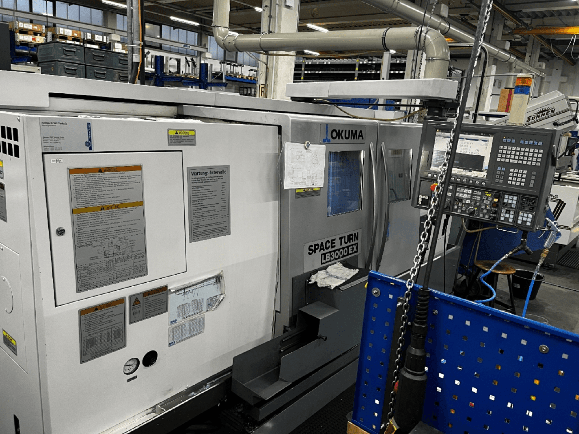 Горизонтальный токарный станок Okuma LB3000 EX, вид спереди, панель управления и информация по технике безопасности сбоку.