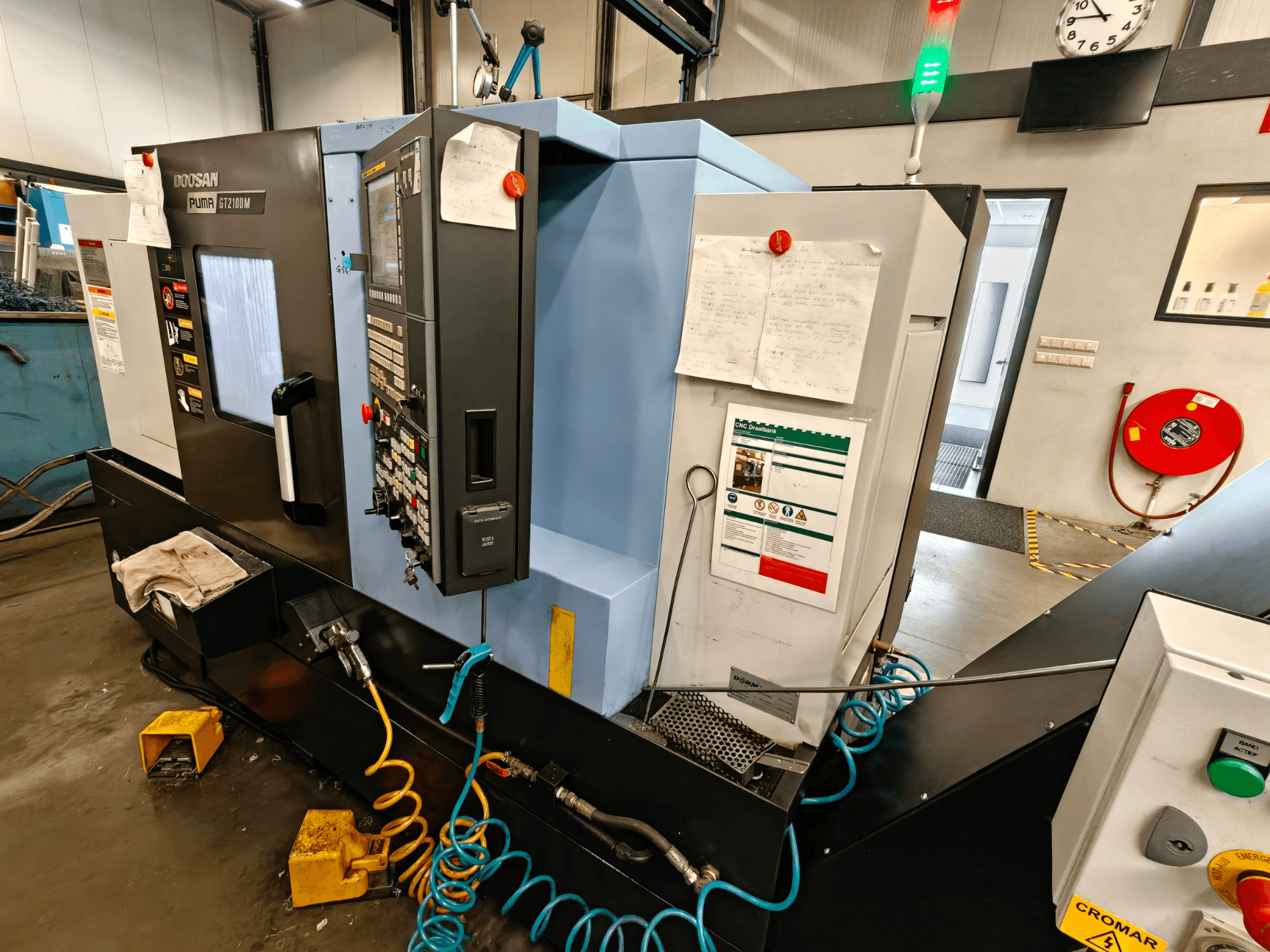 Вид спереди горизонтального токарного станка DOOSAN Puma GT 2100M с панелью управления, элементами безопасности и указаниями по техническому обслуживанию.