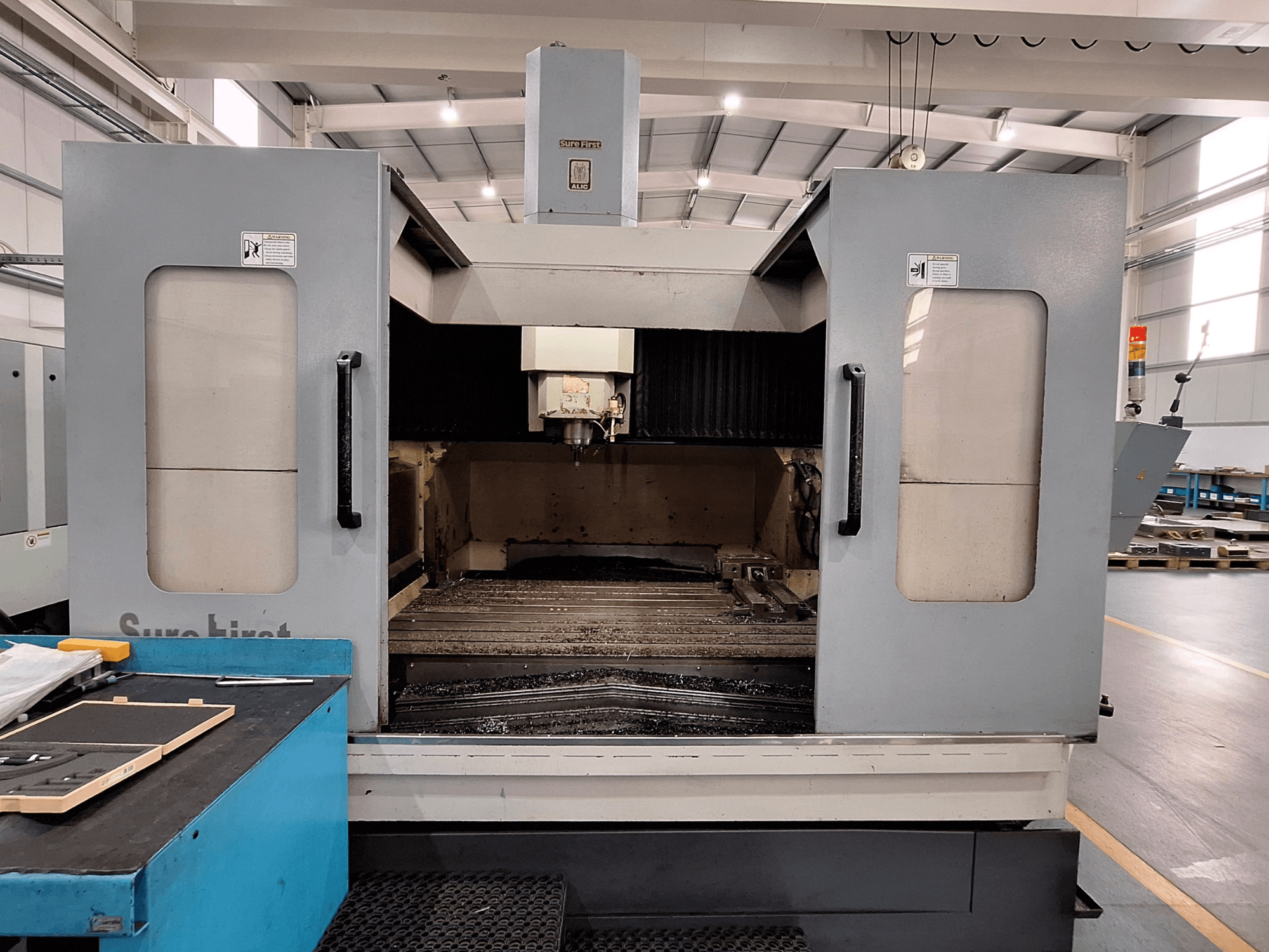 Вертикальный обрабатывающий центр Sure First QM-1836, вид спереди на инструментальную головку и пустую рабочую зону, современная промышленная обстановка.