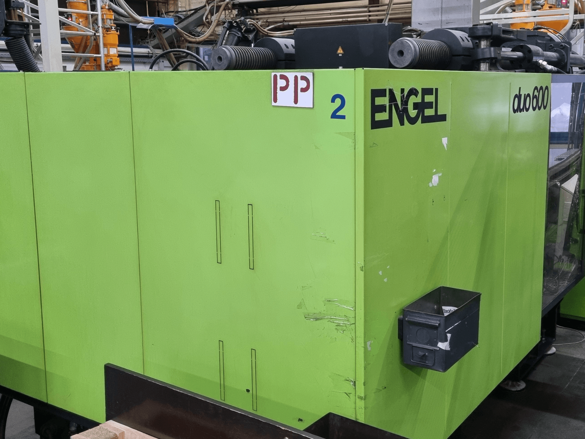 Гидравлическая термопластавтомат Engel duo 600, зелёного цвета, вид спереди, с обозначенными деталями и ящиком для хранения материалов.