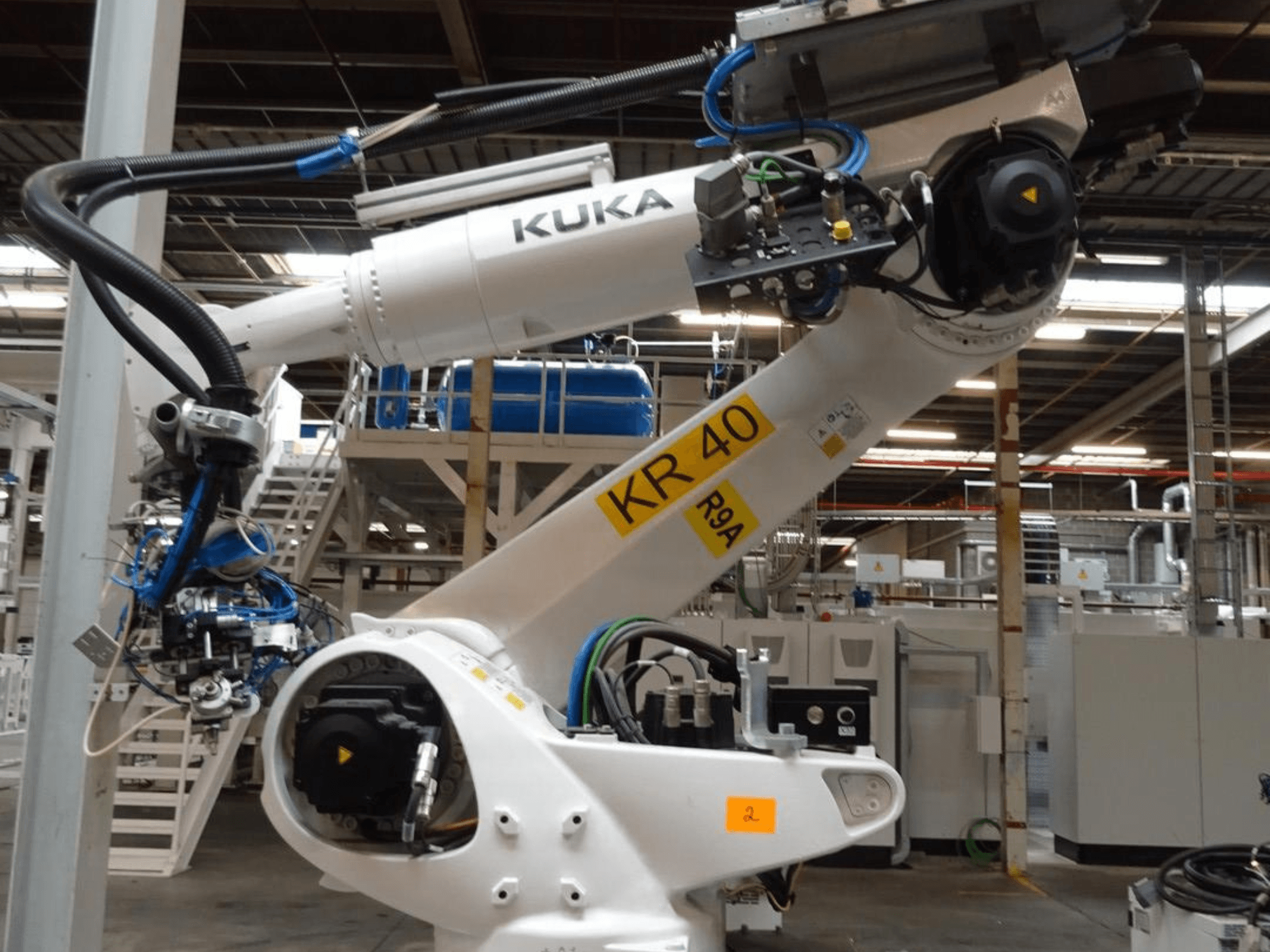 Роботизированная рука KUKA KR 120 R3100-2 в боковом ракурсе, с панелью управления и механическими компонентами, в промышленной обстановке.