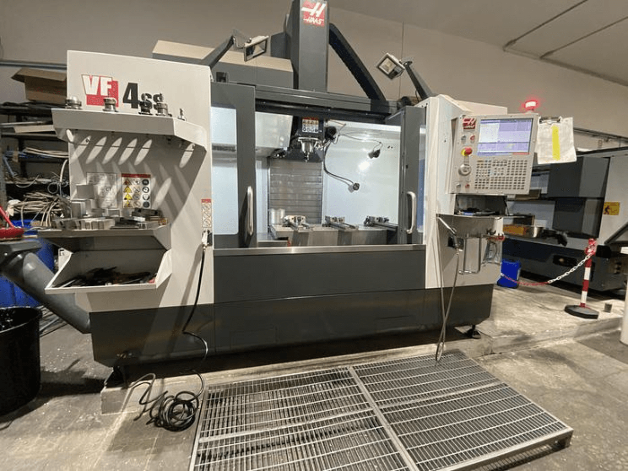 Фрезерный станок с ЧПУ Haas VF-4SS, вид спереди, с хранилищем инструментов, панелью управления и видимой рабочей зоной в мастерской.
