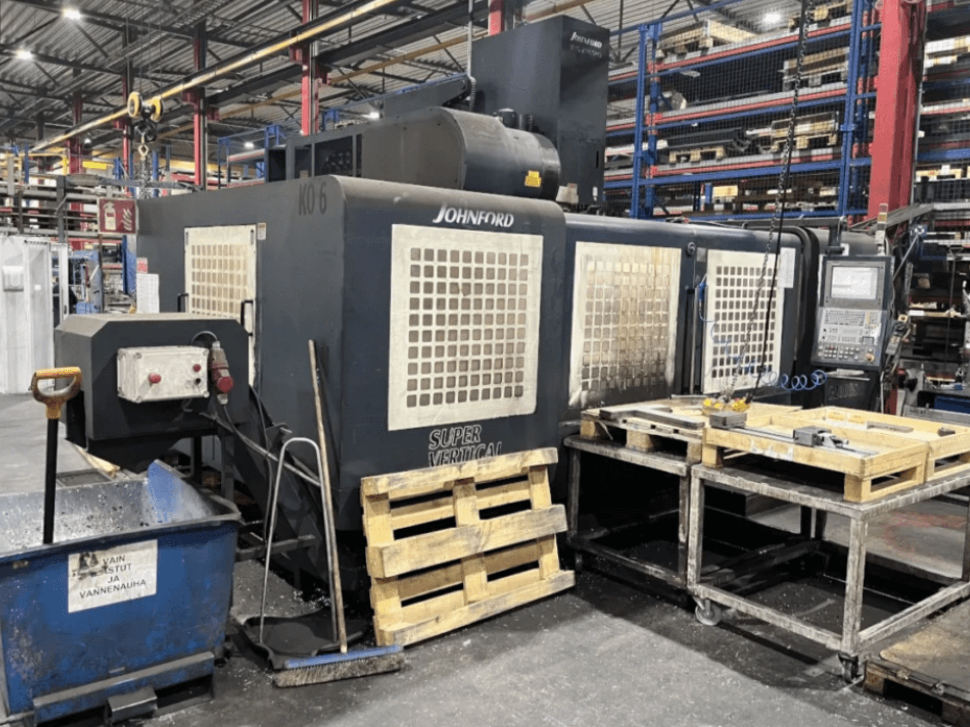 Вертикально-фрезерный станок Johnford Super Vertical на заводе, вид сбоку с панелью управления, поддонами и очистительным оборудованием рядом.