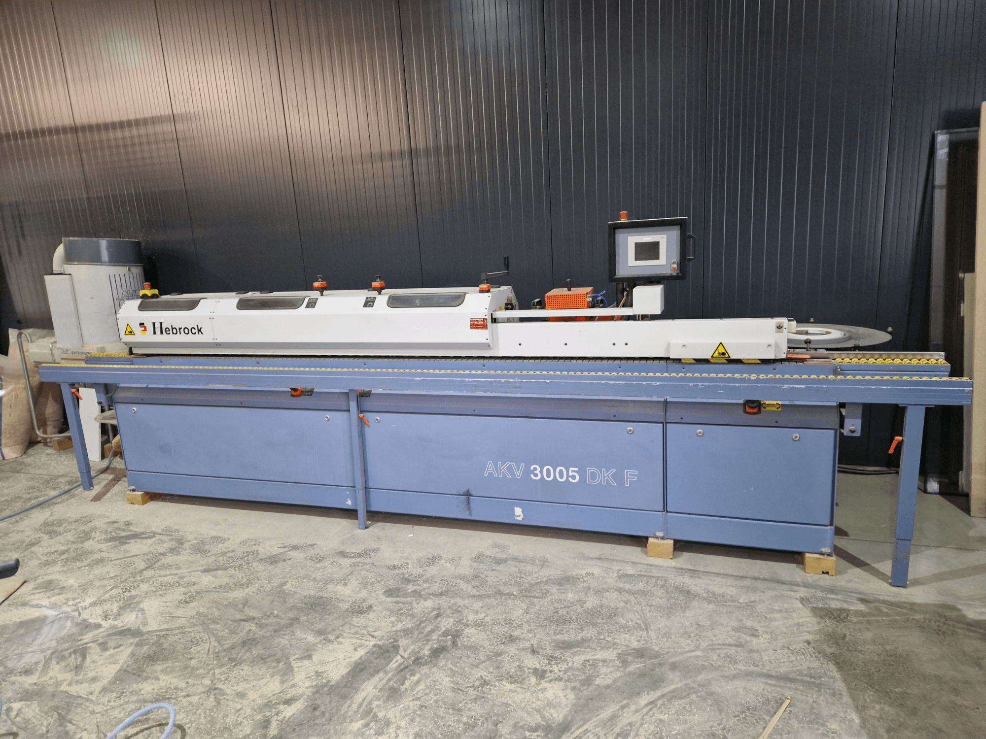 Кромкооблицовочный станок HEBROCK AKV 3005 DK-F, вид спереди, с панелью управления, подающей лентой и регулируемыми настройками.