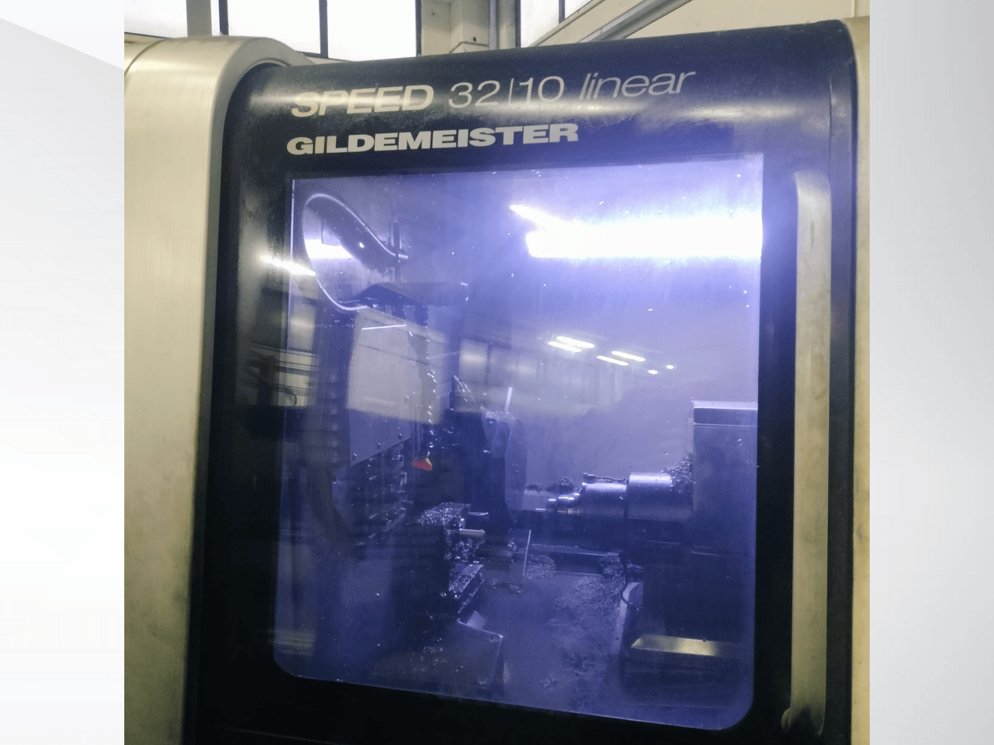 Линейный станок с ЧПУ Gildemeister SPEED 3210 вид спереди, демонстрирующий внутренние компоненты и жидкую охлаждающую жидкость в работе.