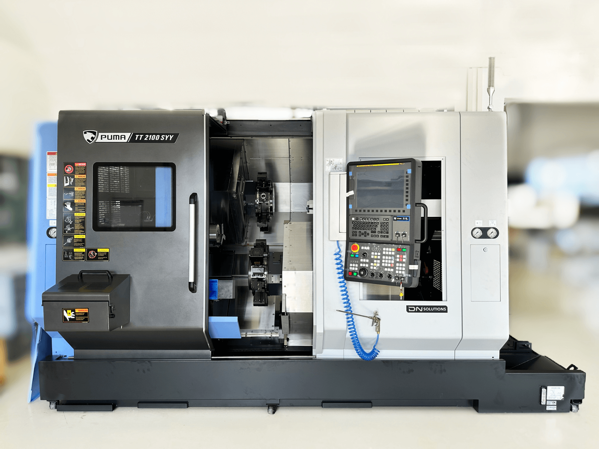 Токарно-фрезерный центр DN SOLUTIONS PUMA TT2100SYY вид спереди, с панелью управления и видимыми внутренними компонентами.