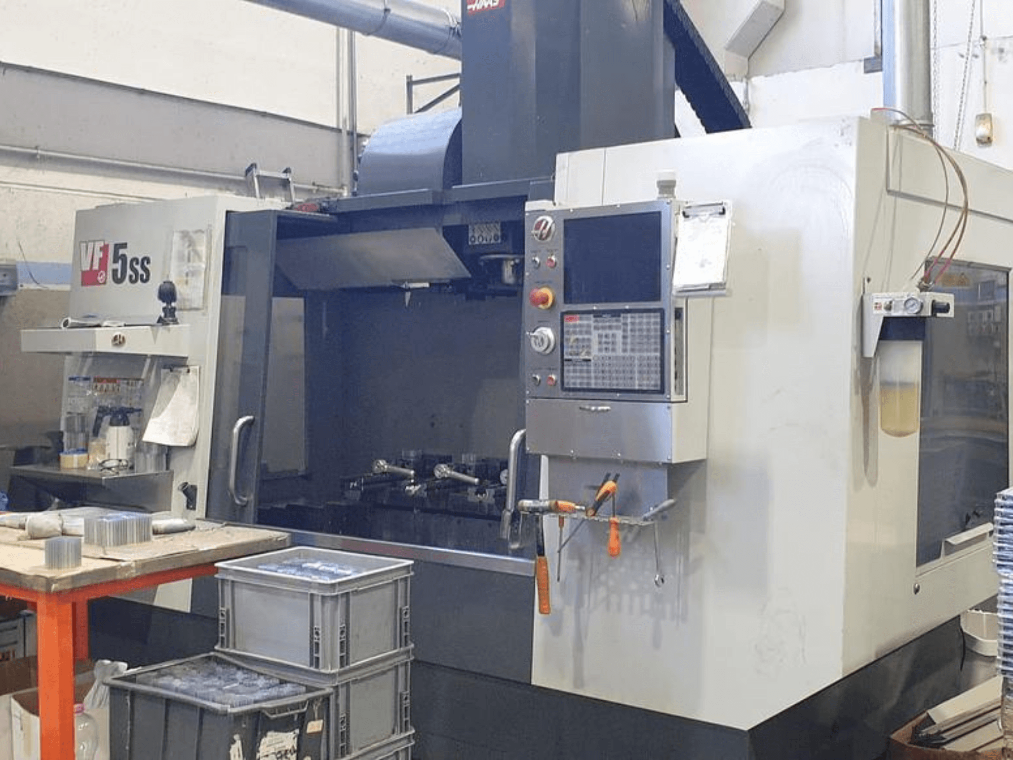 Вертикальный обрабатывающий центр HAAS VF-5SS на виде спереди, панель управления, рабочая зона и контейнеры для хранения.